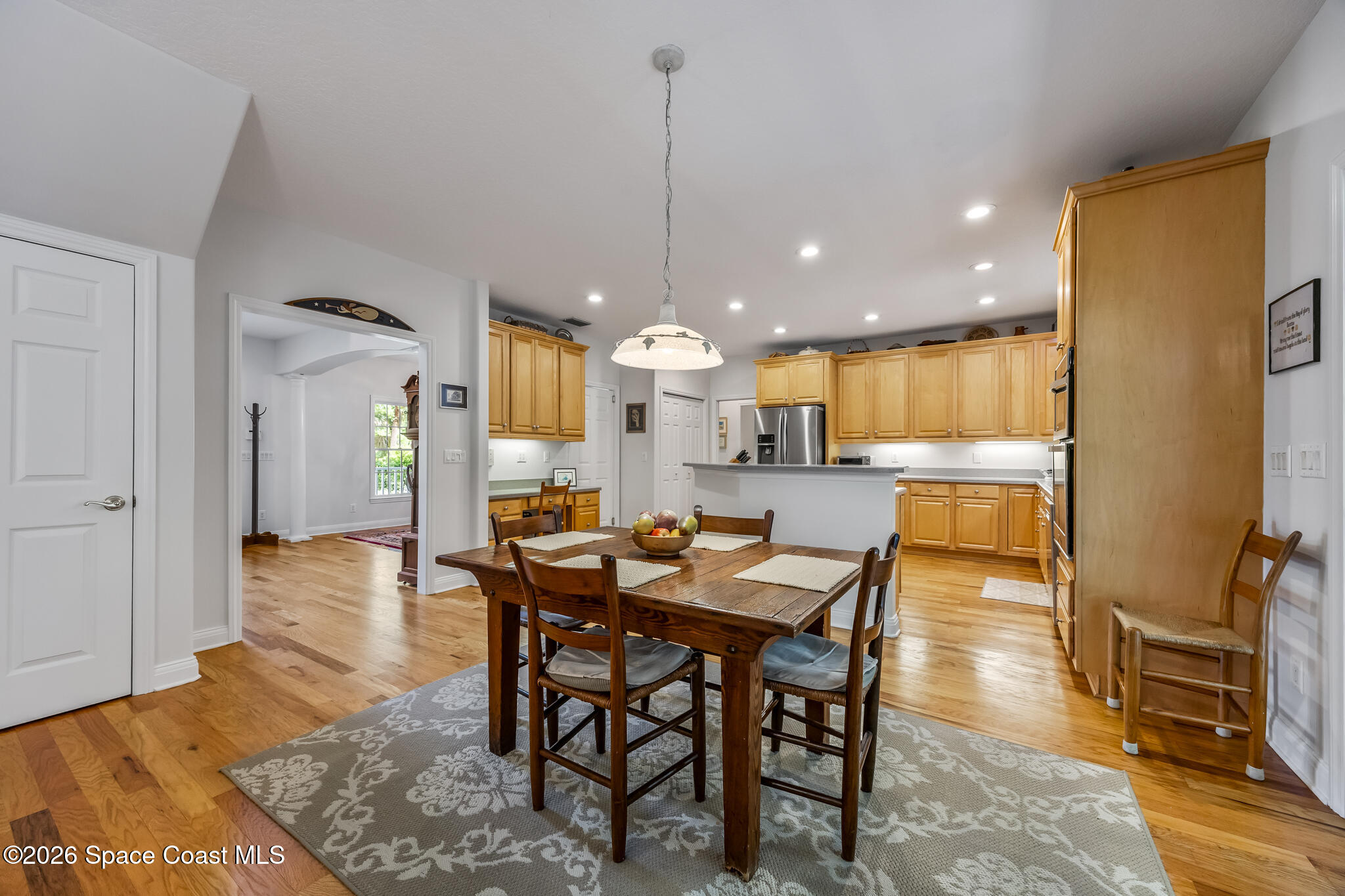 Dining area with a dark wood table beside a kitchen with honey-colored cabinets.