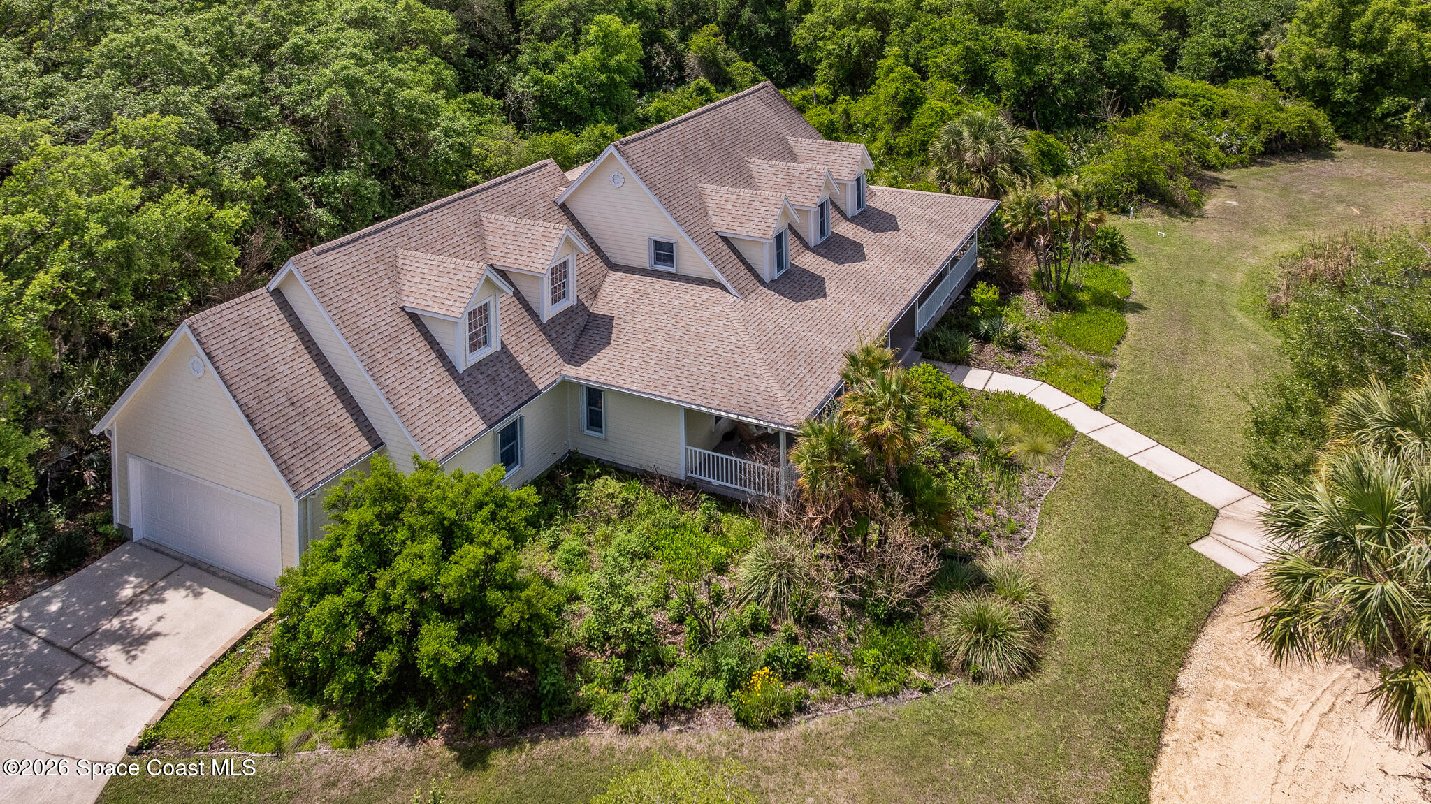 Aerial view of a large home with multiple roof dormers, an attached garage, and landscaped grounds.