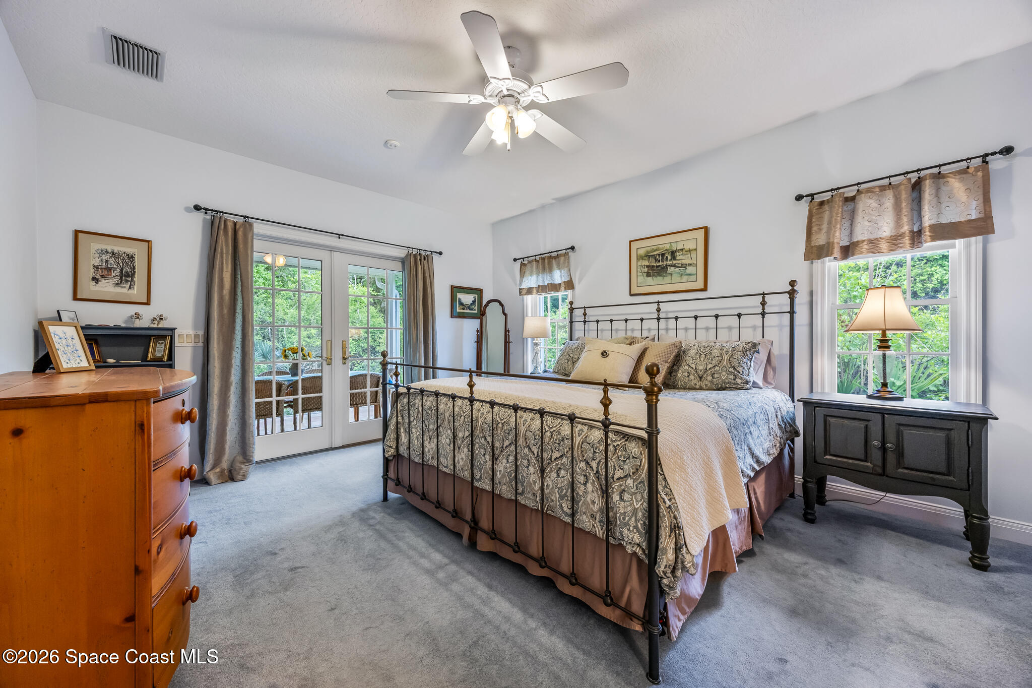 Furnished bedroom with a black metal bed and French doors overlooking greenery.