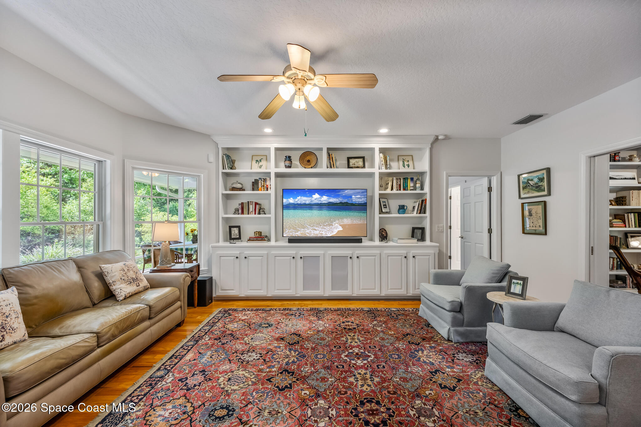 Living room with built-in entertainment shelving, large windows, and a patterned rug.