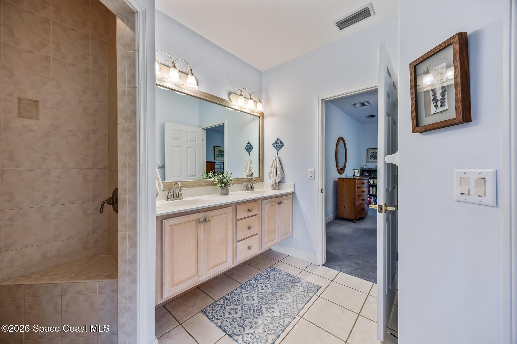 Bathroom with a double vanity and tiled shower, viewed from the doorway.