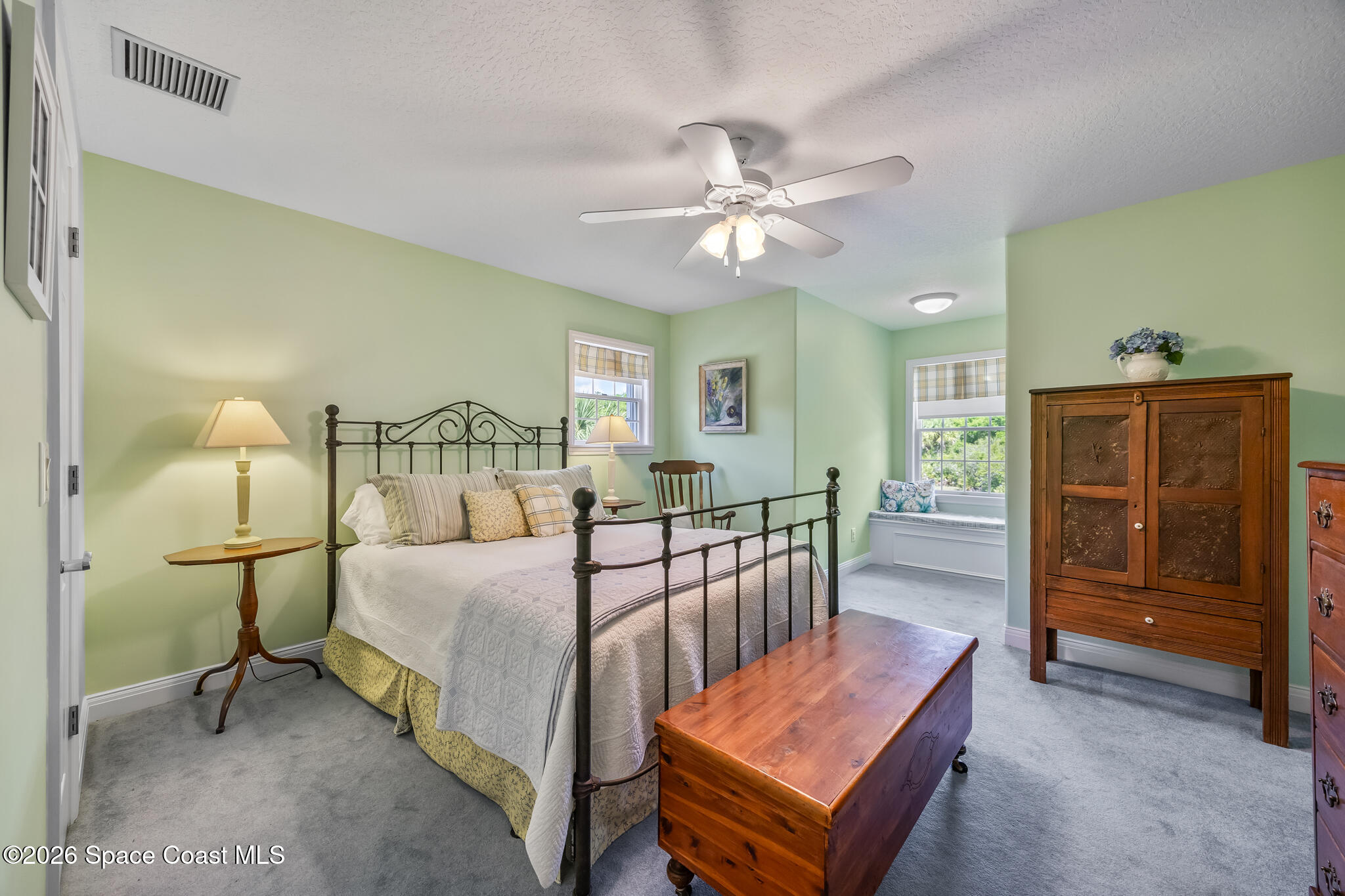 Furnished bedroom with pale green walls, a dark metal bed, and a wooden chest at its foot.