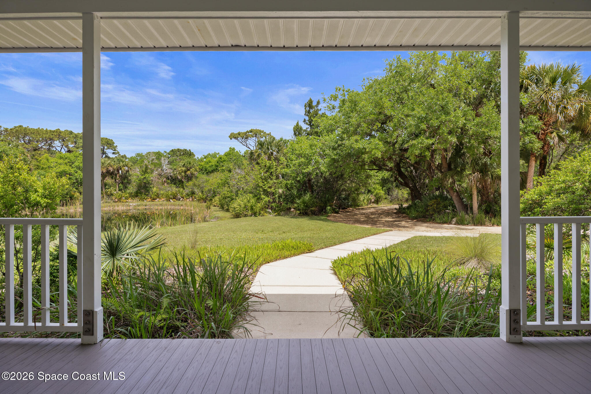 Covered porch overlooking a landscaped yard, pond, and mature trees along a curved walkway.