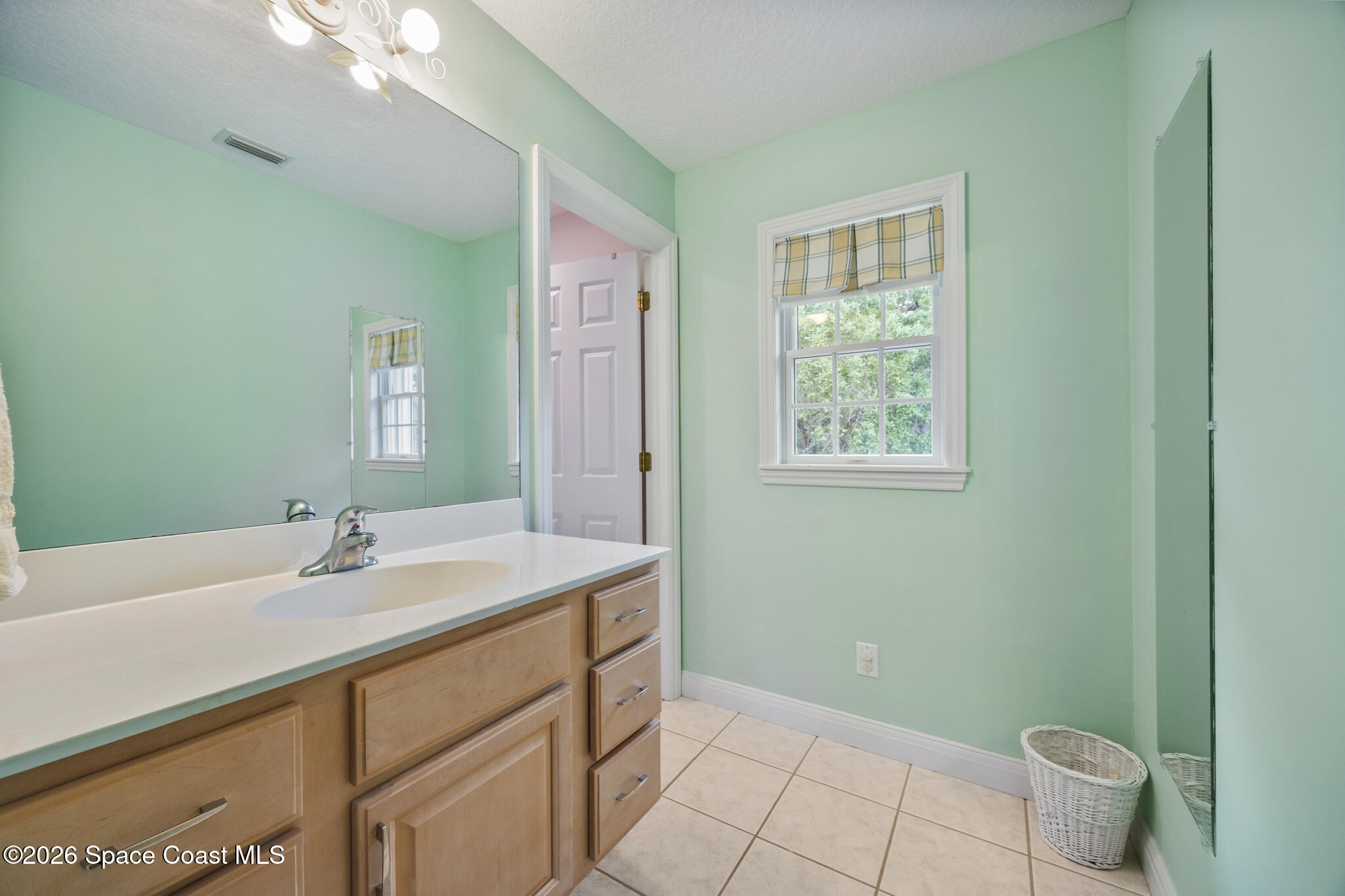 Bathroom with a light-wood vanity, white countertop, and window with a plaid shade.