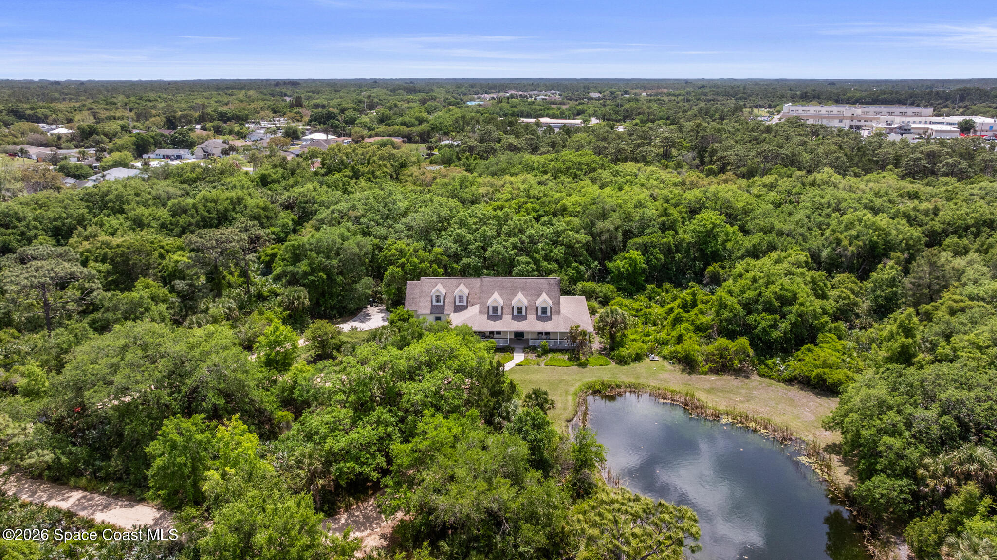 Aerial view of a home surrounded by woods, with a pond in the front yard.