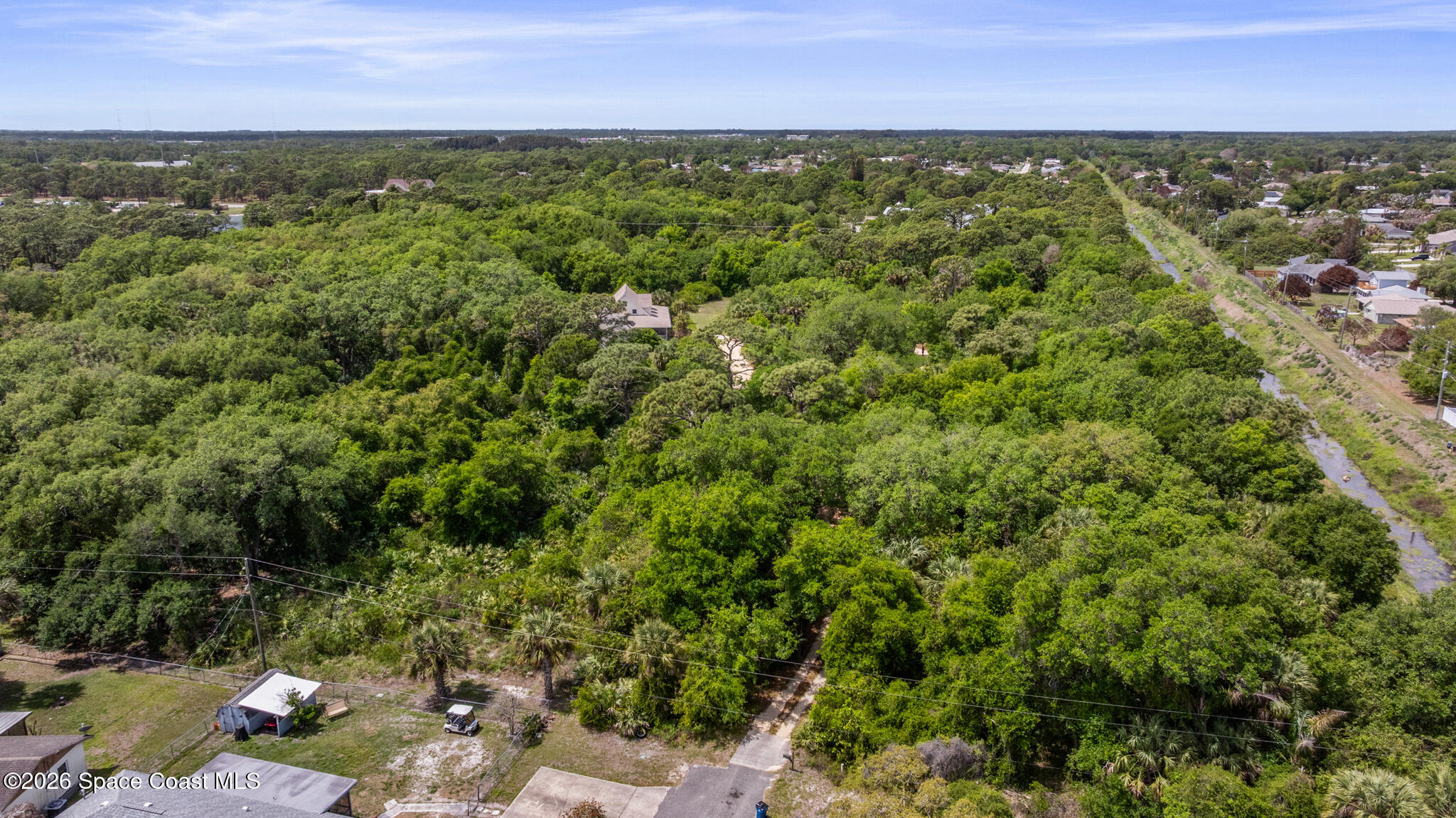Aerial view of a wooded property with nearby homes and a cleared corridor along one side.