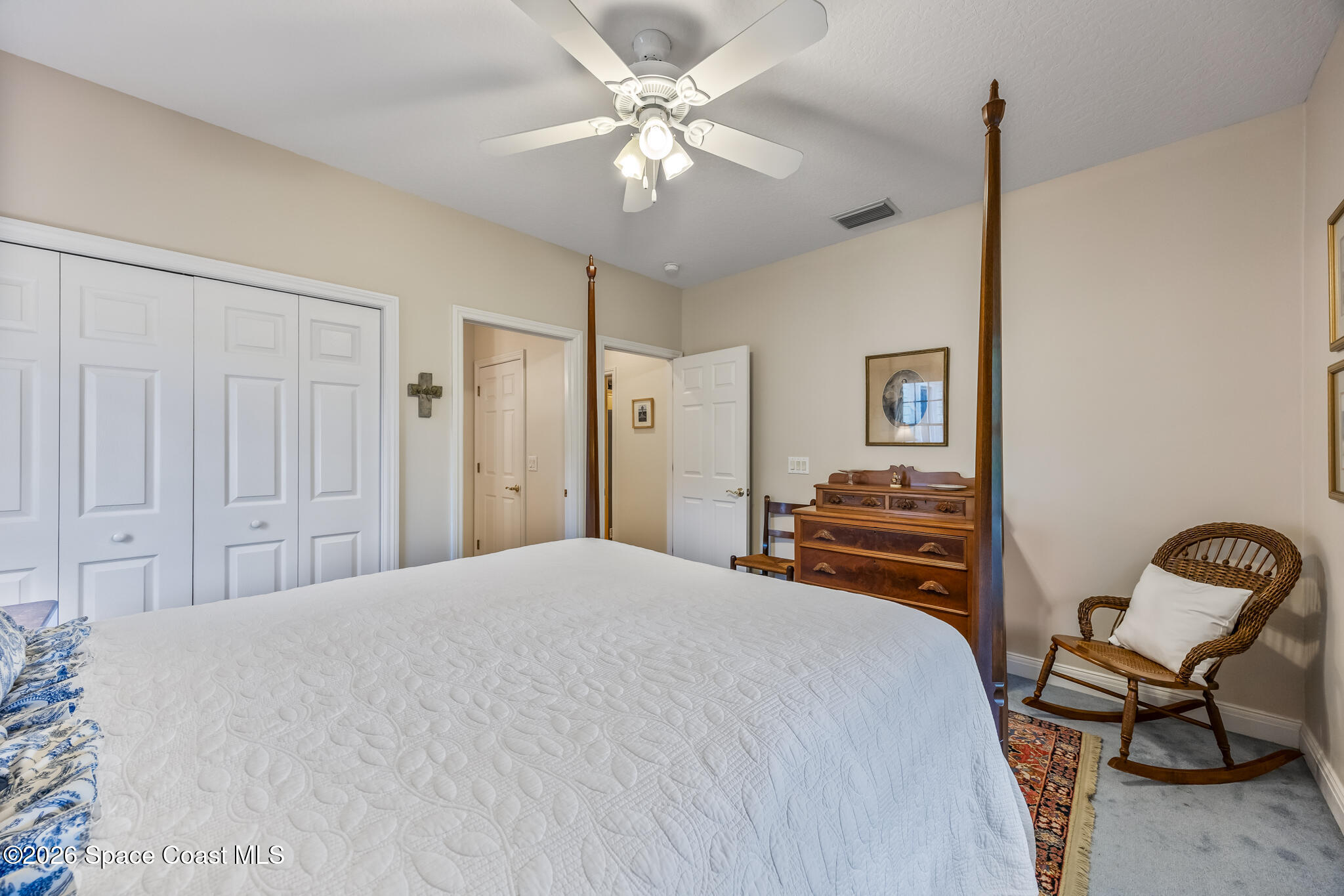Bedroom with a white quilted bed, dark wood four-poster frame, and wicker rocking chair.