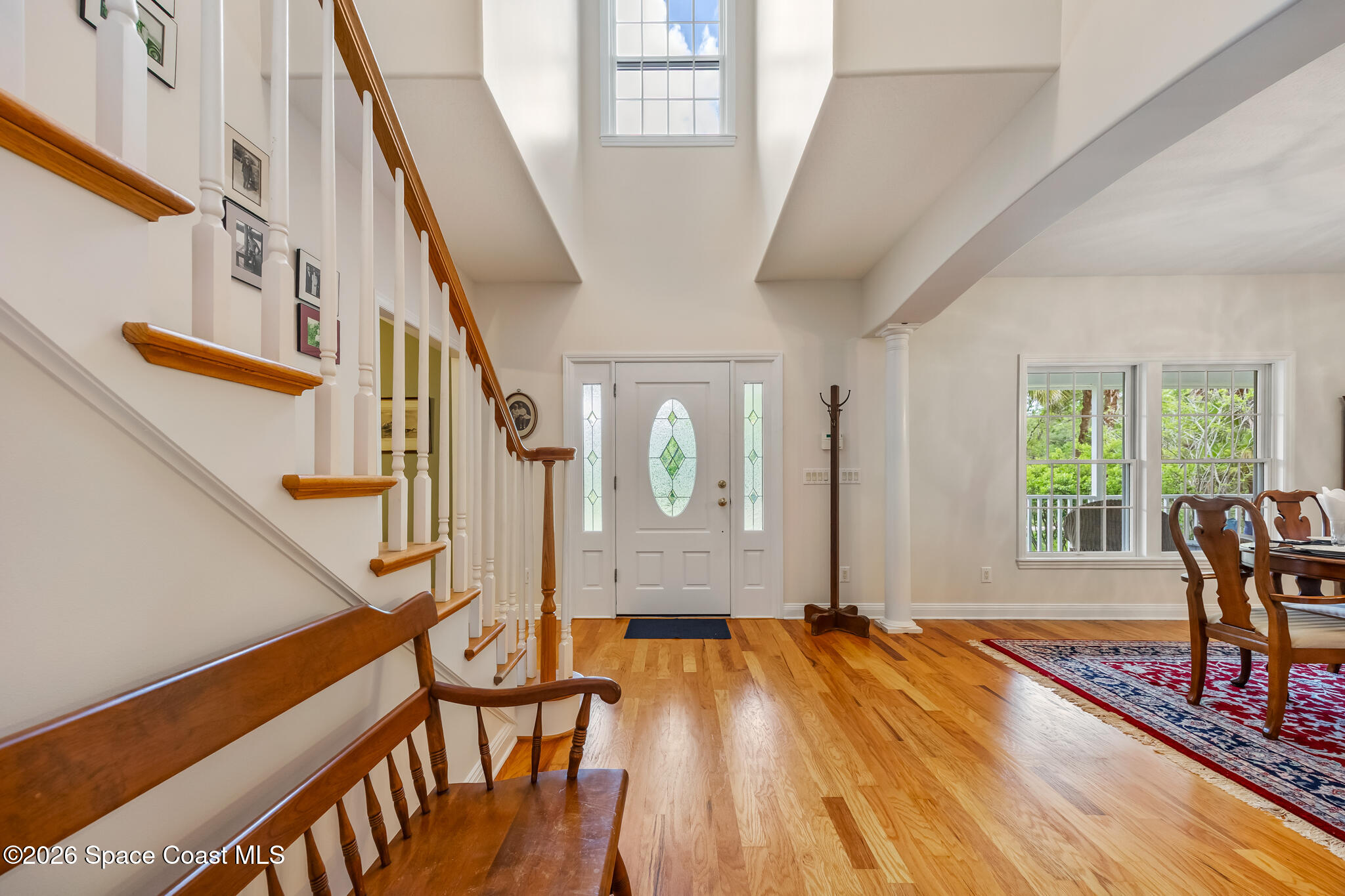 Two-story foyer with a glass-paneled front door, wooden staircase, and hardwood floors beside the dining area.