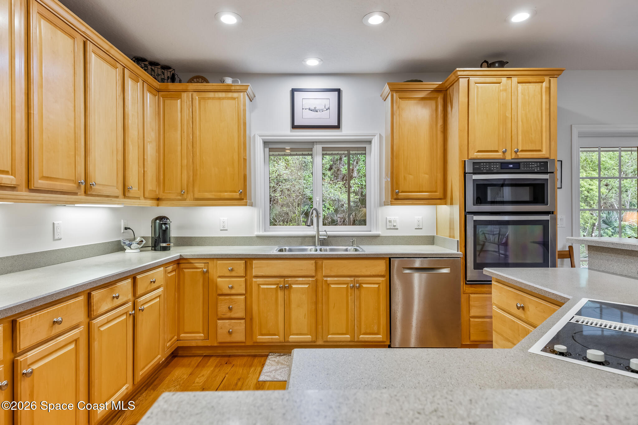 Kitchen with honey-colored wood cabinets, light countertops, and a sink beneath a window.