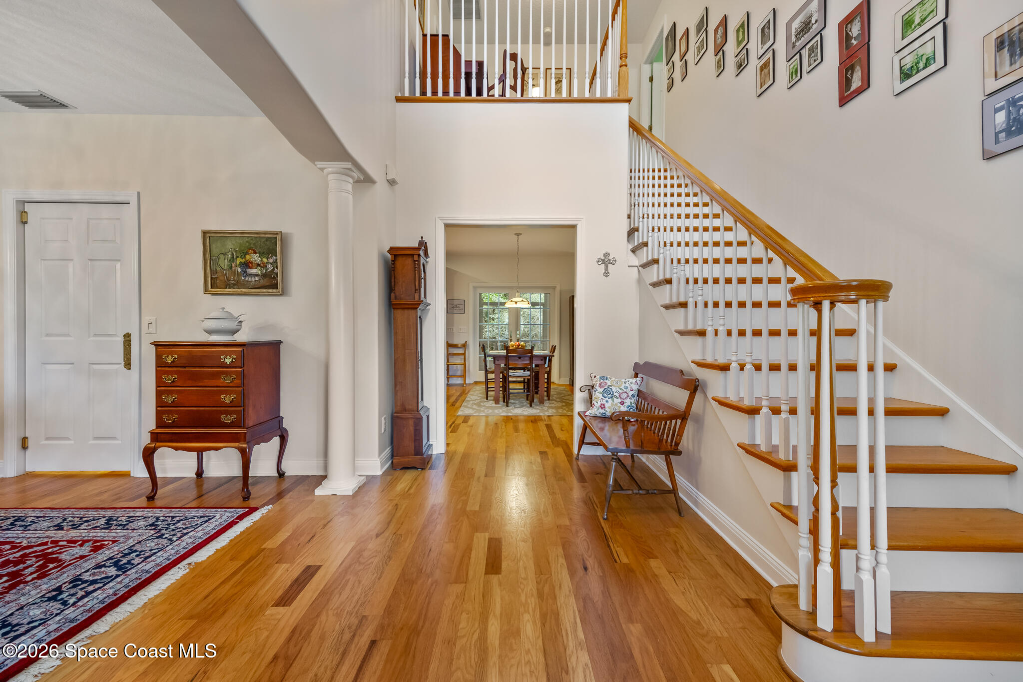Two-story foyer with a curved wood-and-white staircase, hardwood floors, and dining room beyond.