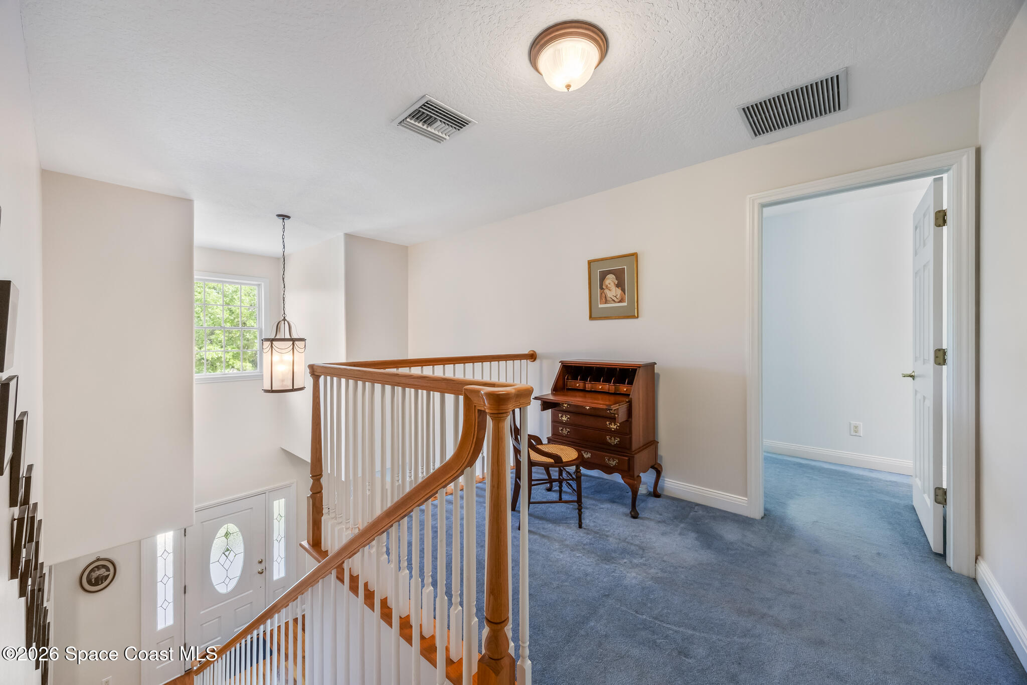 Upstairs landing with blue carpet, a wooden stair railing, and an antique writing desk.