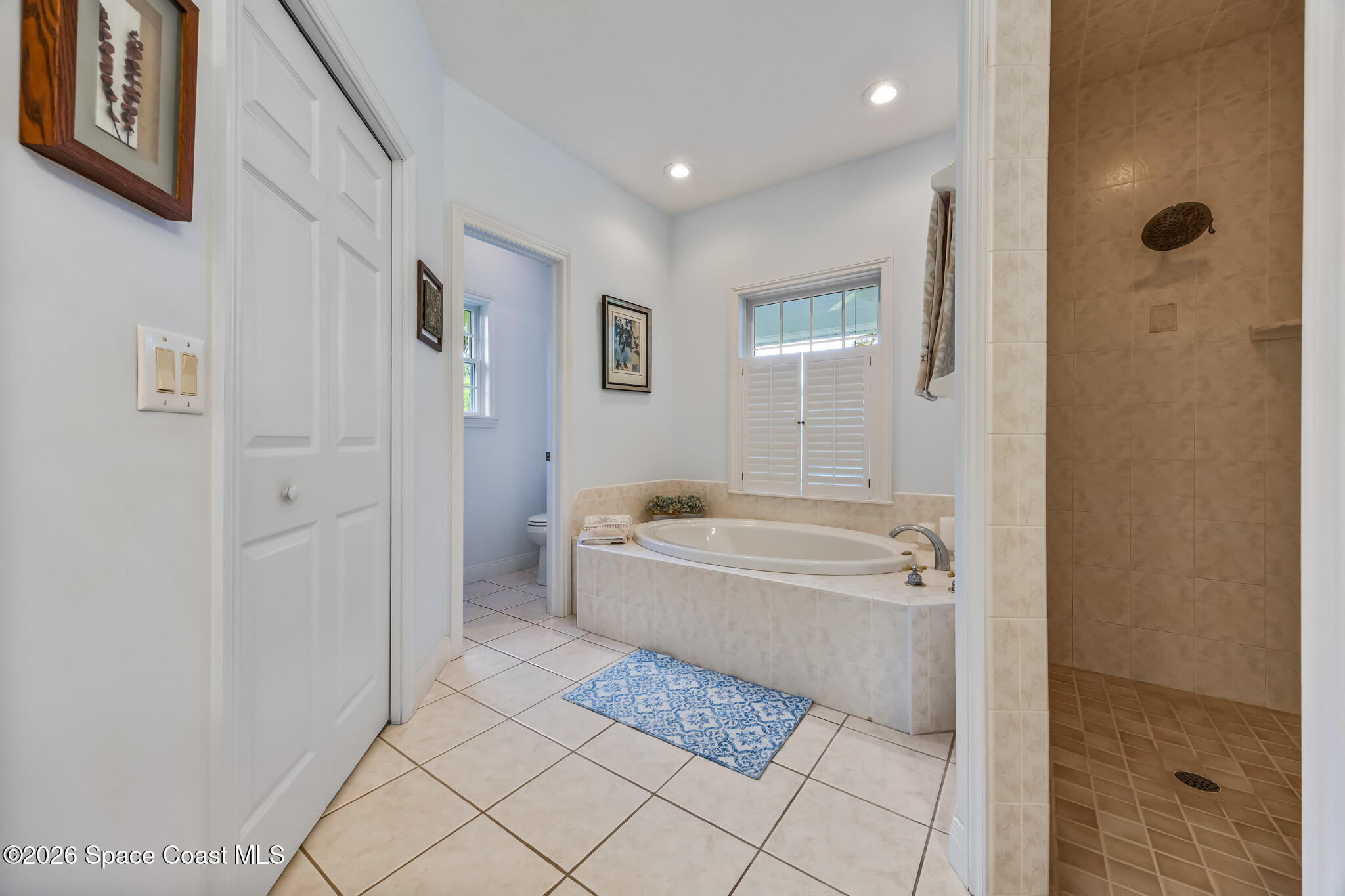 Bathroom with a built-in soaking tub beneath shutters and an adjacent tiled walk-in shower.