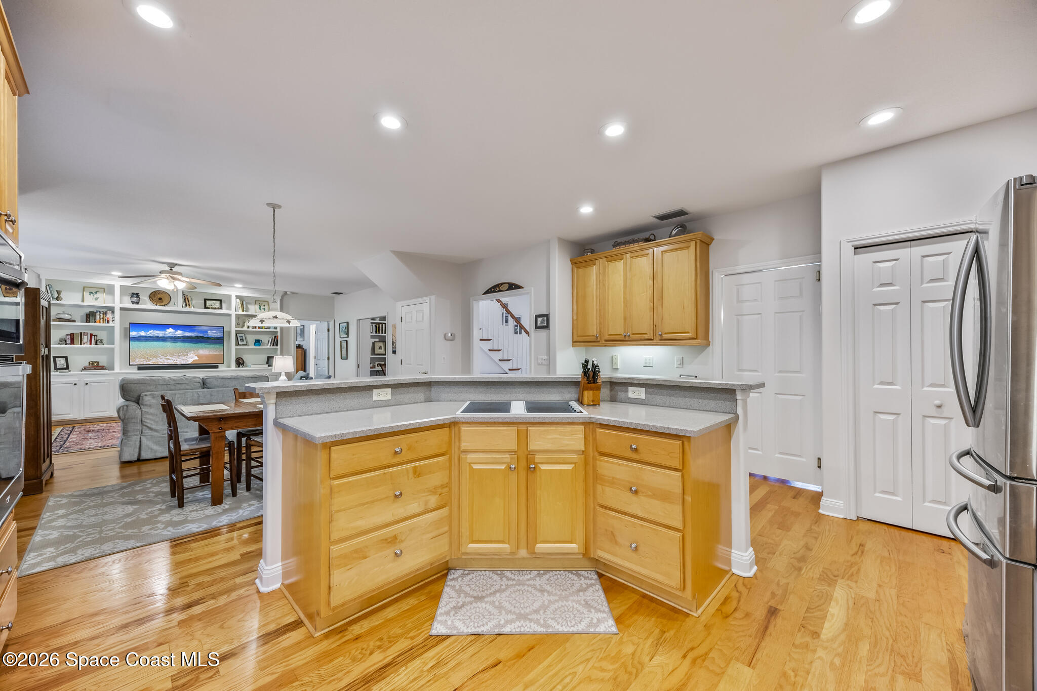 Open-plan kitchen with honey-colored cabinets and a peninsula overlooking the dining and living areas.