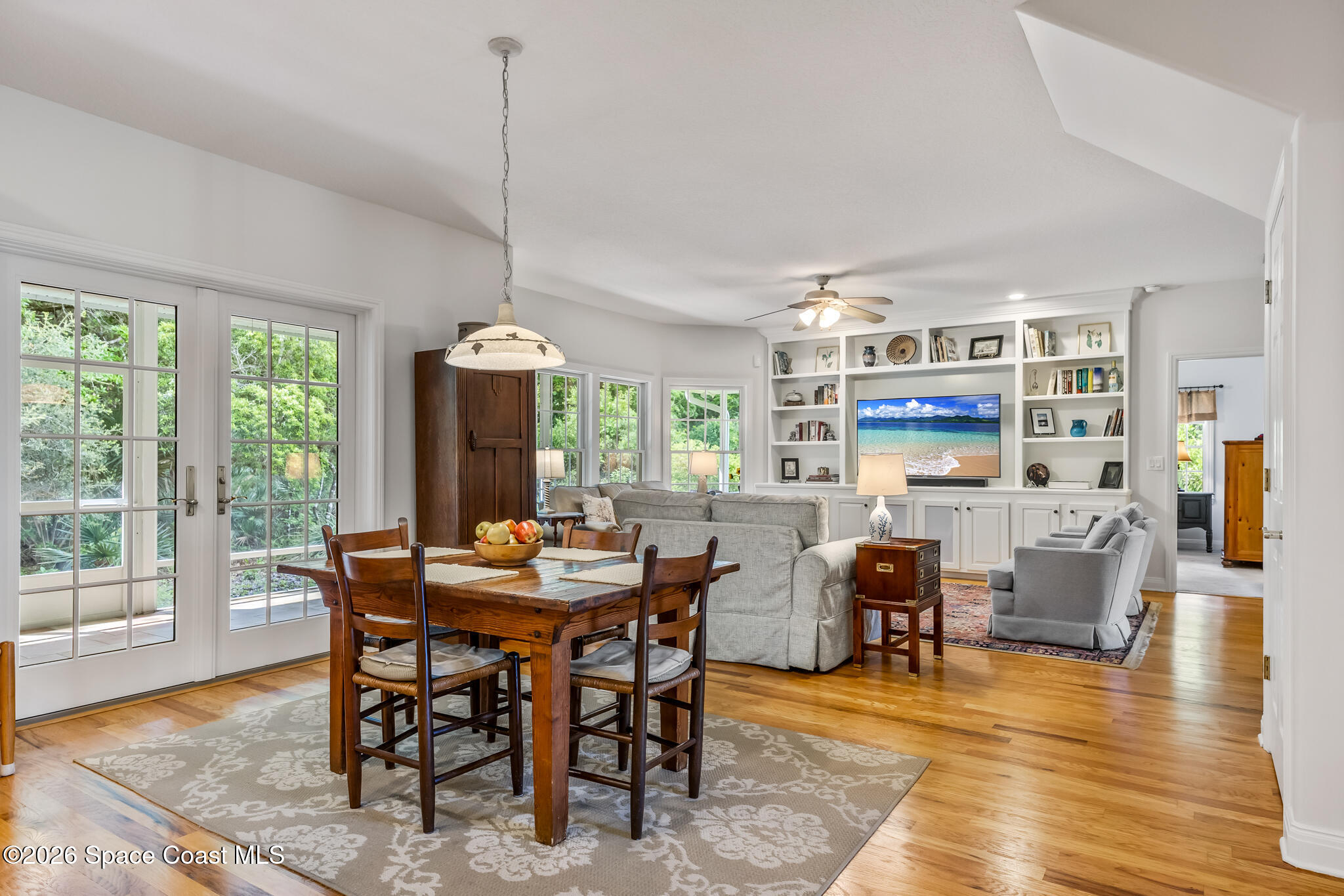 Open-plan dining and living room with hardwood floors, French doors, and built-in shelving.