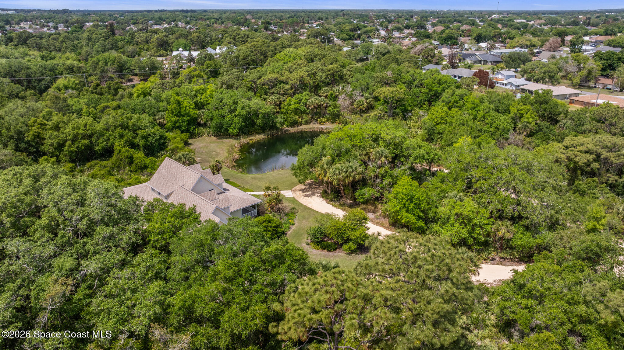Aerial view of a wooded property with a home, pond, and sandy drive.