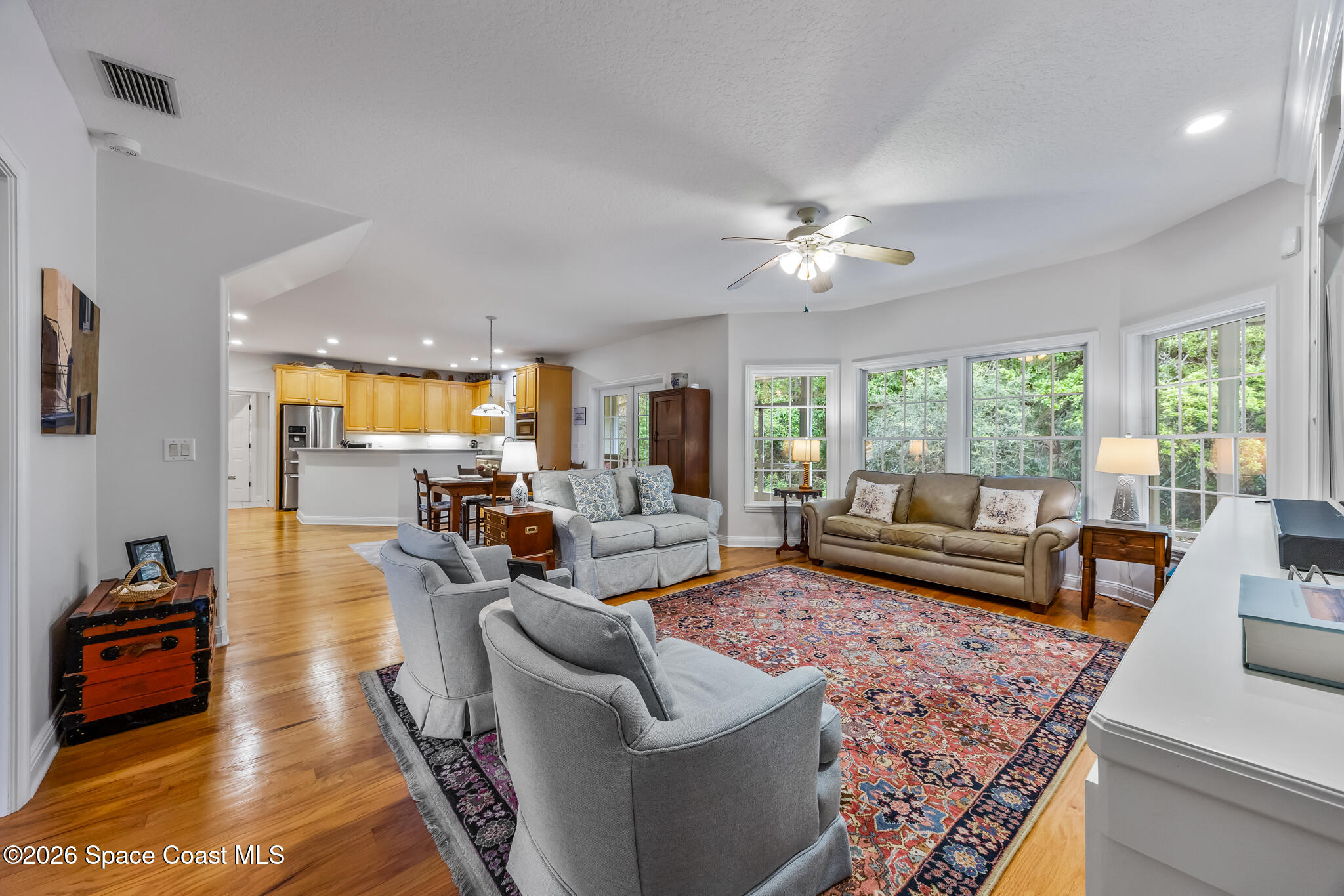 Living room with gray armchairs, a tan sofa, patterned rug, and open kitchen.