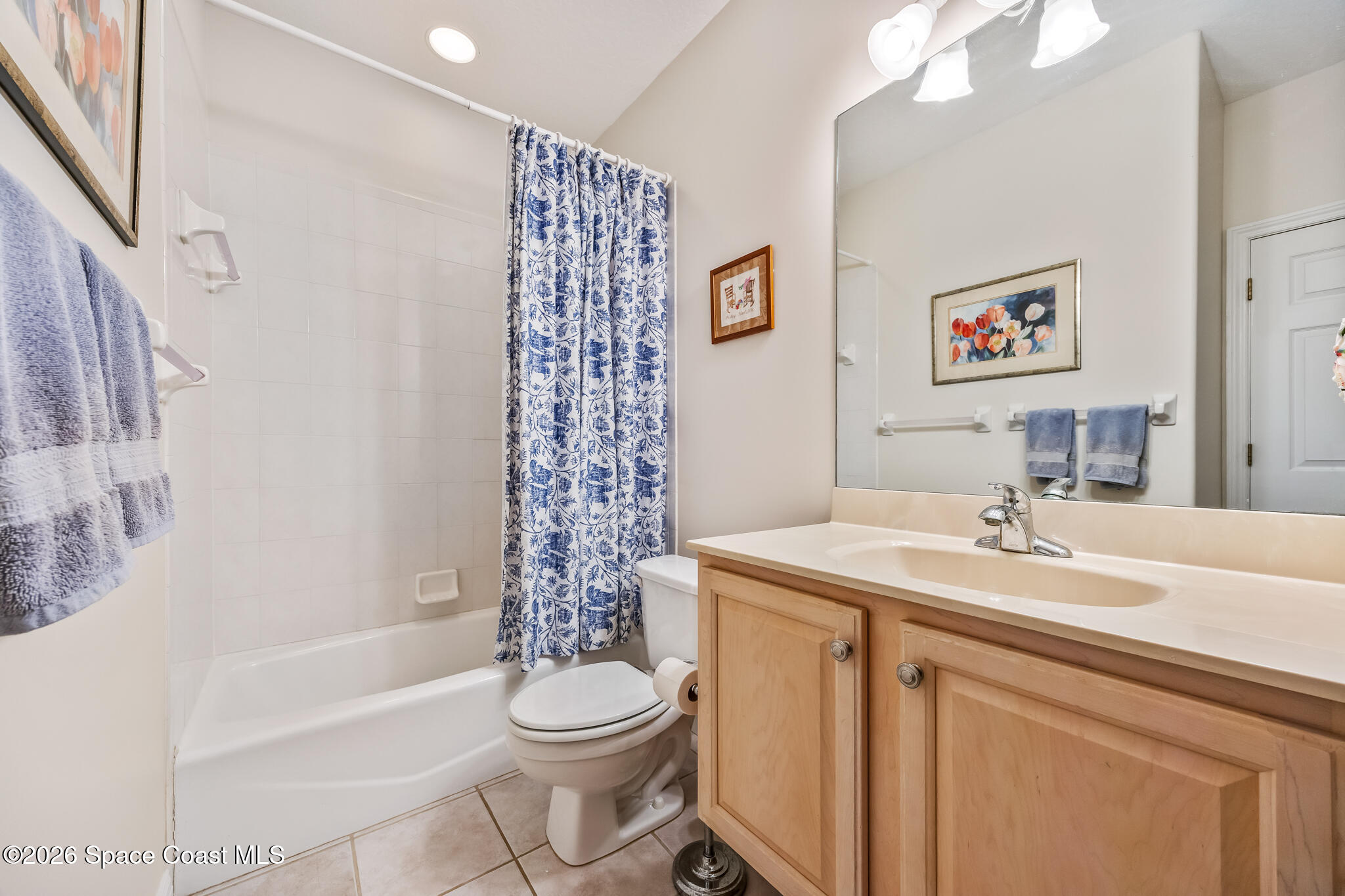 Bathroom with a white tub, patterned blue shower curtain, and light wood vanity.