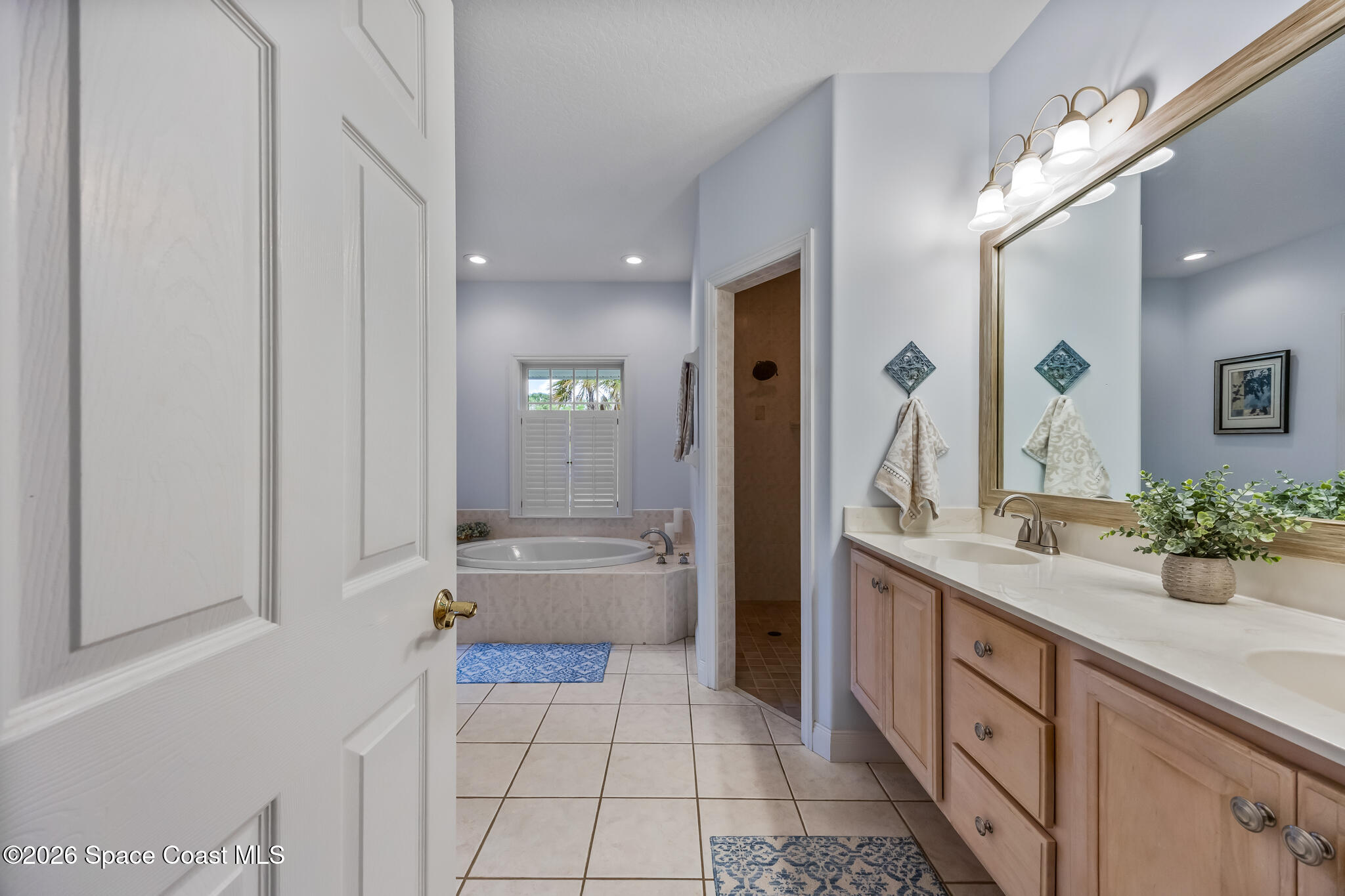 Bathroom with a long wood vanity and mirror, plus a soaking tub beneath a shuttered window.