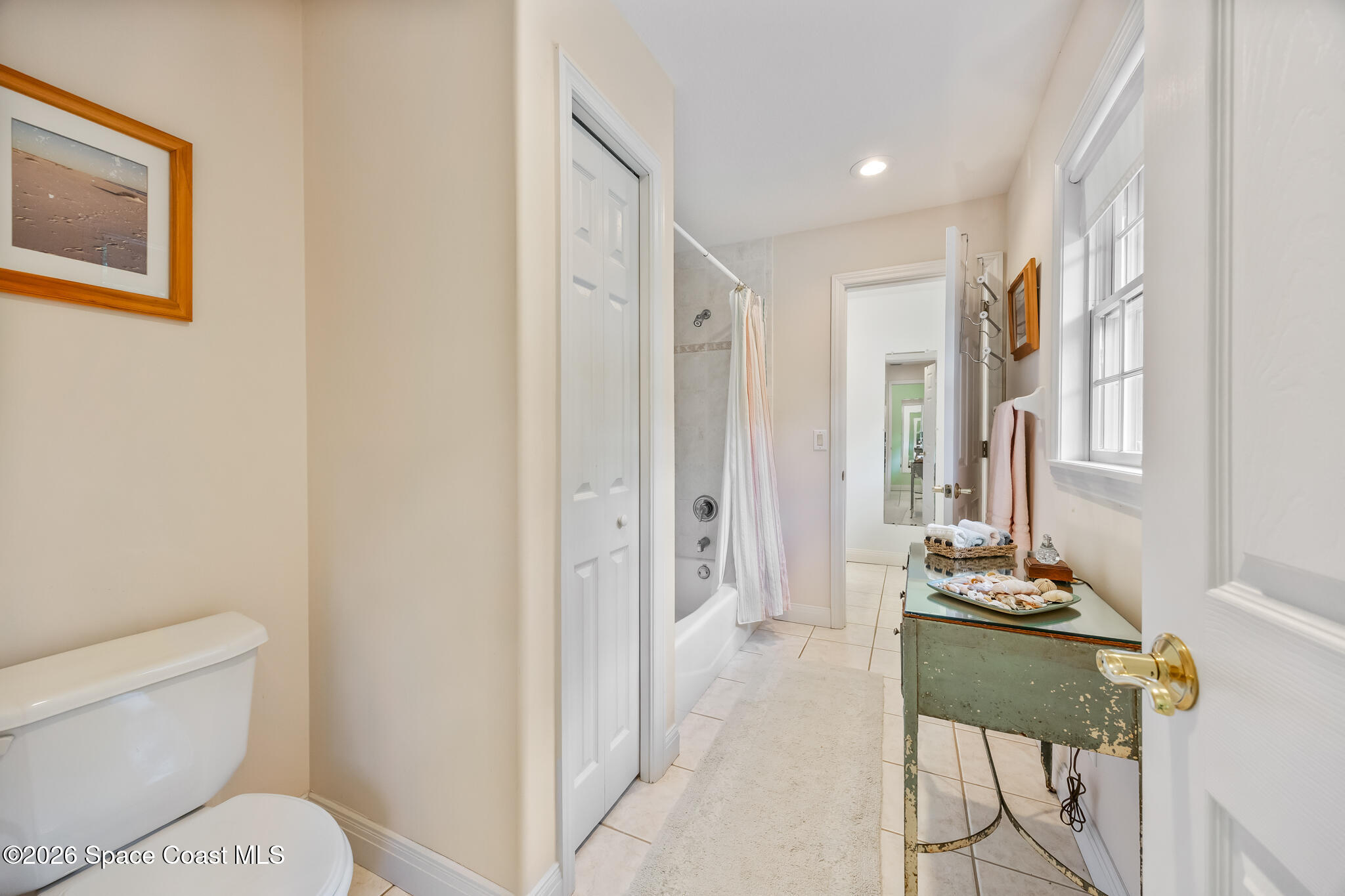 Bathroom with a curtained tub, tiled floor, and distressed green vanity beneath a window.