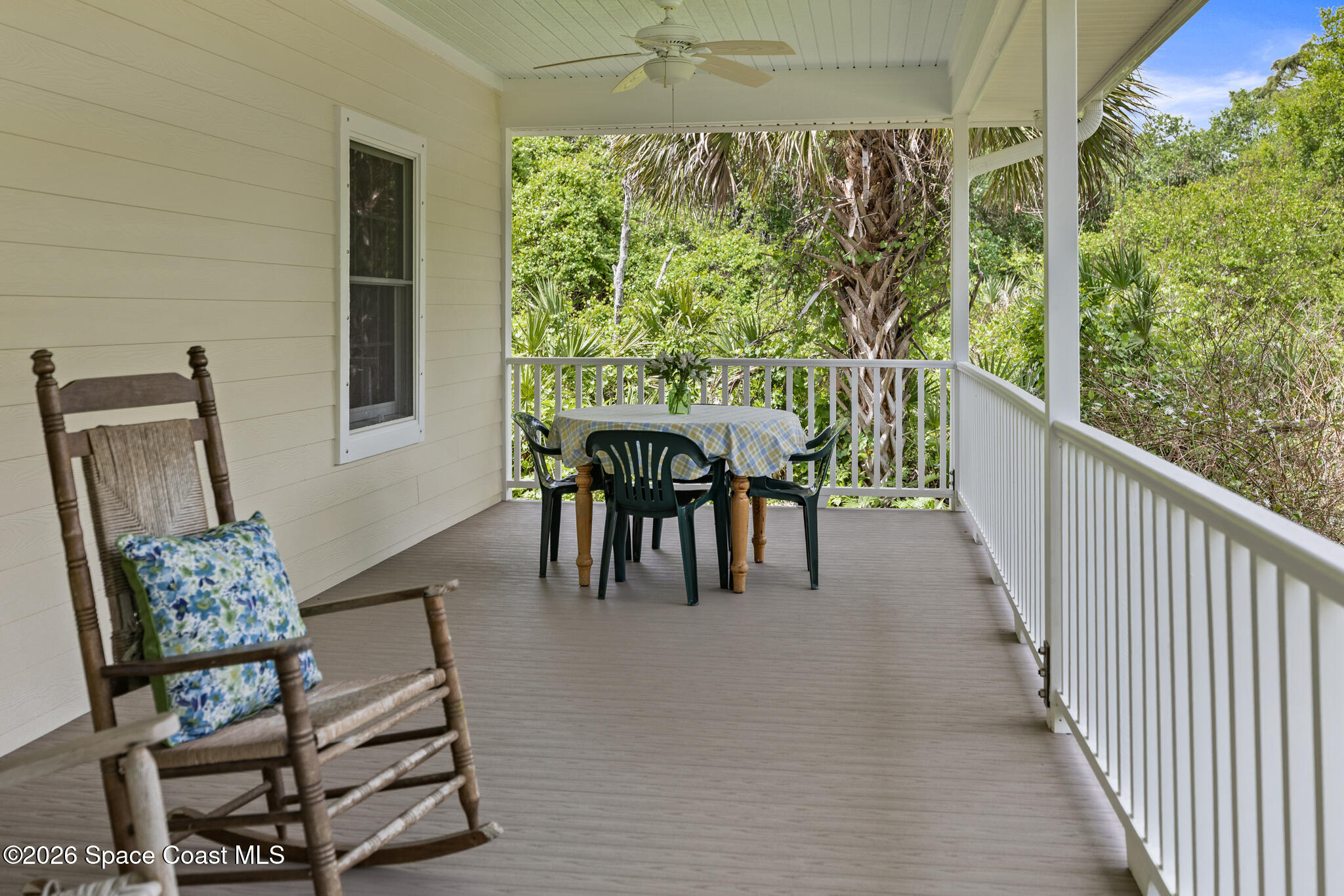 Covered porch with a rocking chair and dining table overlooking tropical greenery.