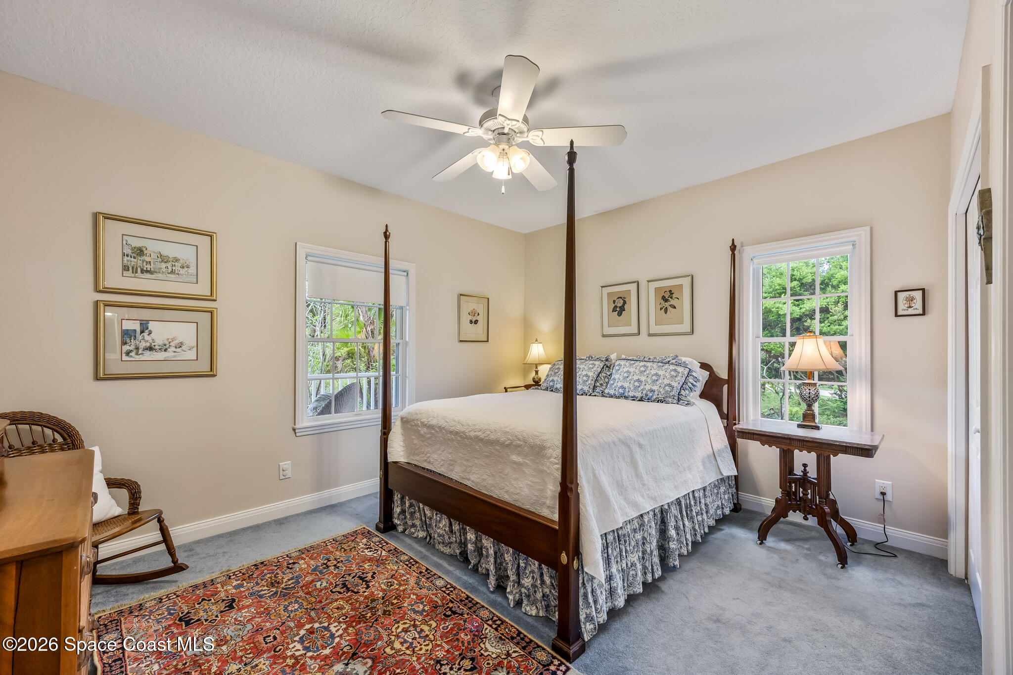 Bedroom with a dark wood four-poster bed, blue patterned pillows, and windows overlooking greenery.