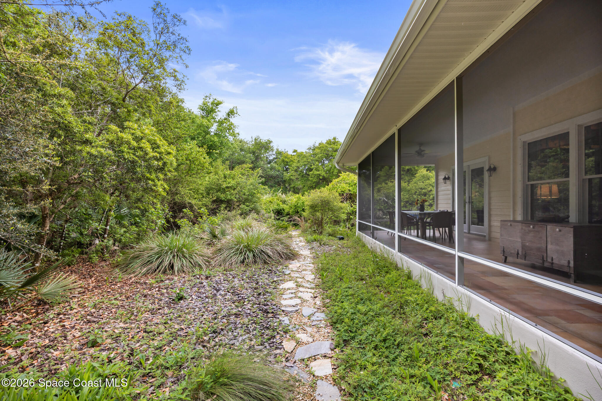 Home’s screened porch beside lush landscaping and a stepping-stone path.