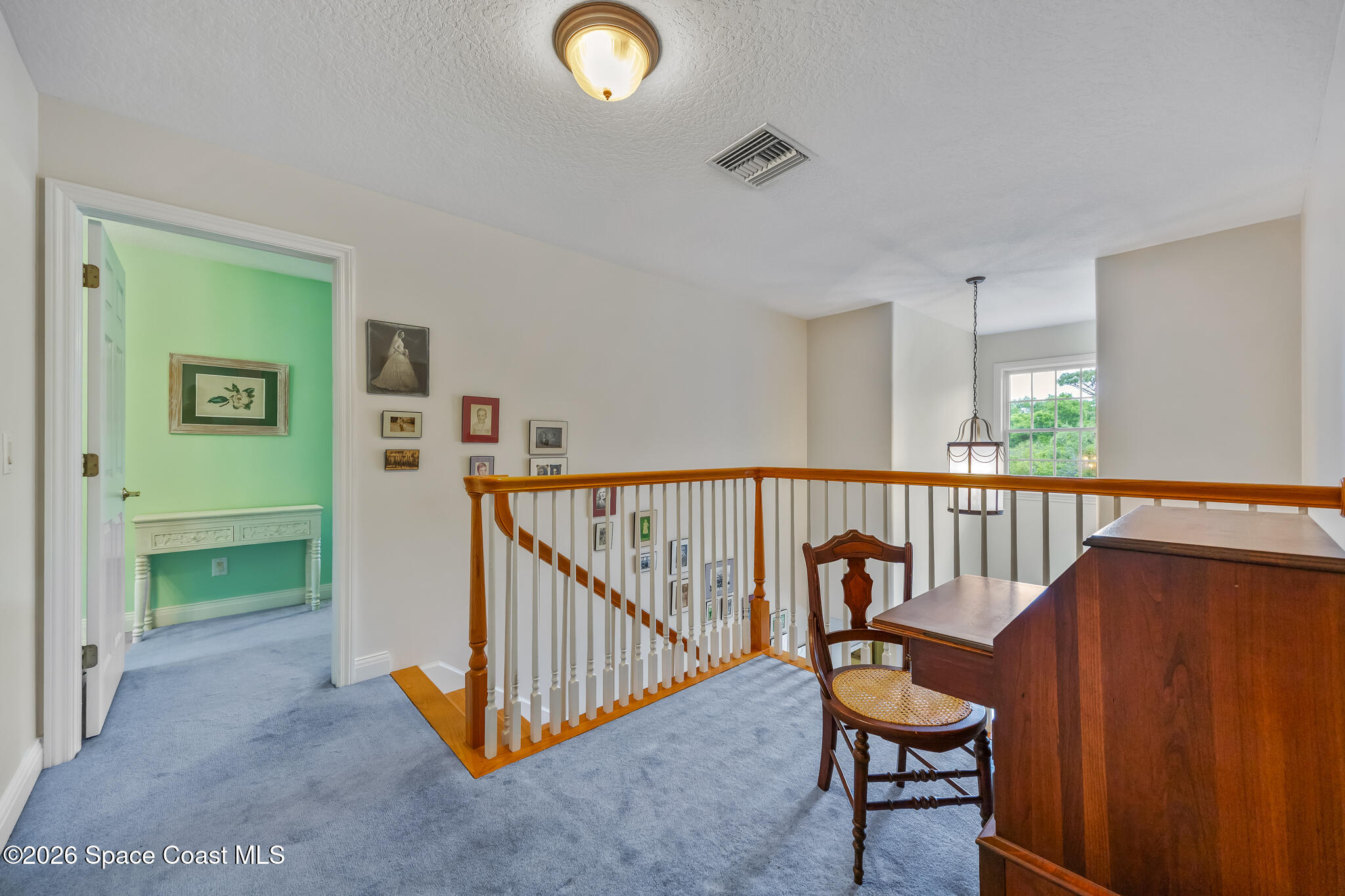 Upstairs landing with blue carpet, wooden railing, and a desk beside an open mint-green room.
