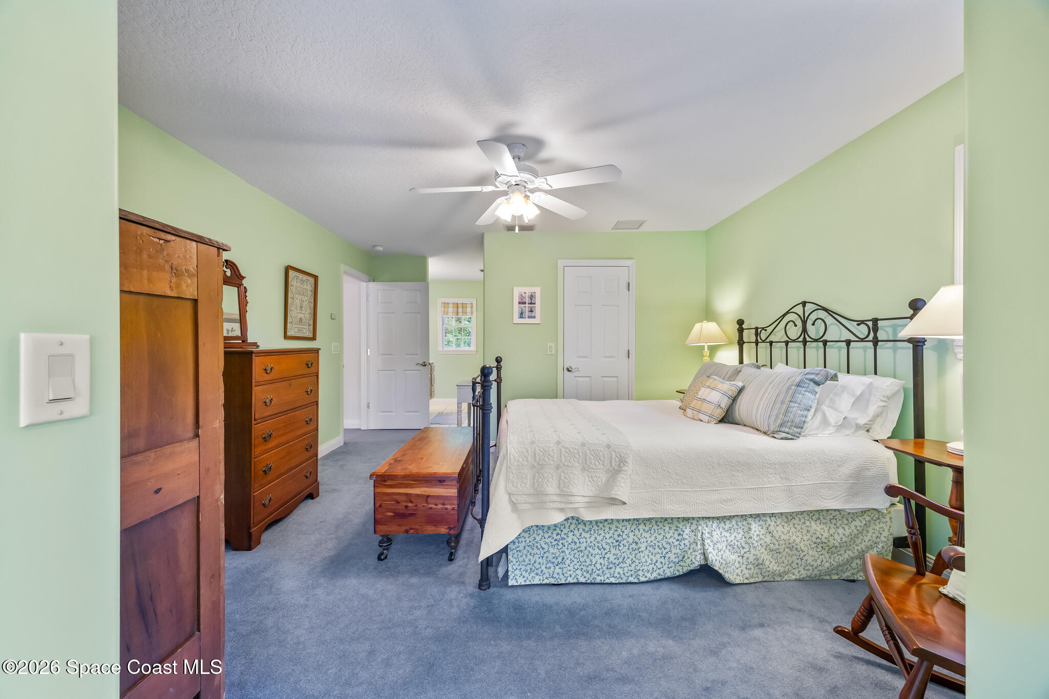 Bedroom with pale green walls, blue carpet, and a white bed beneath a ceiling fan.