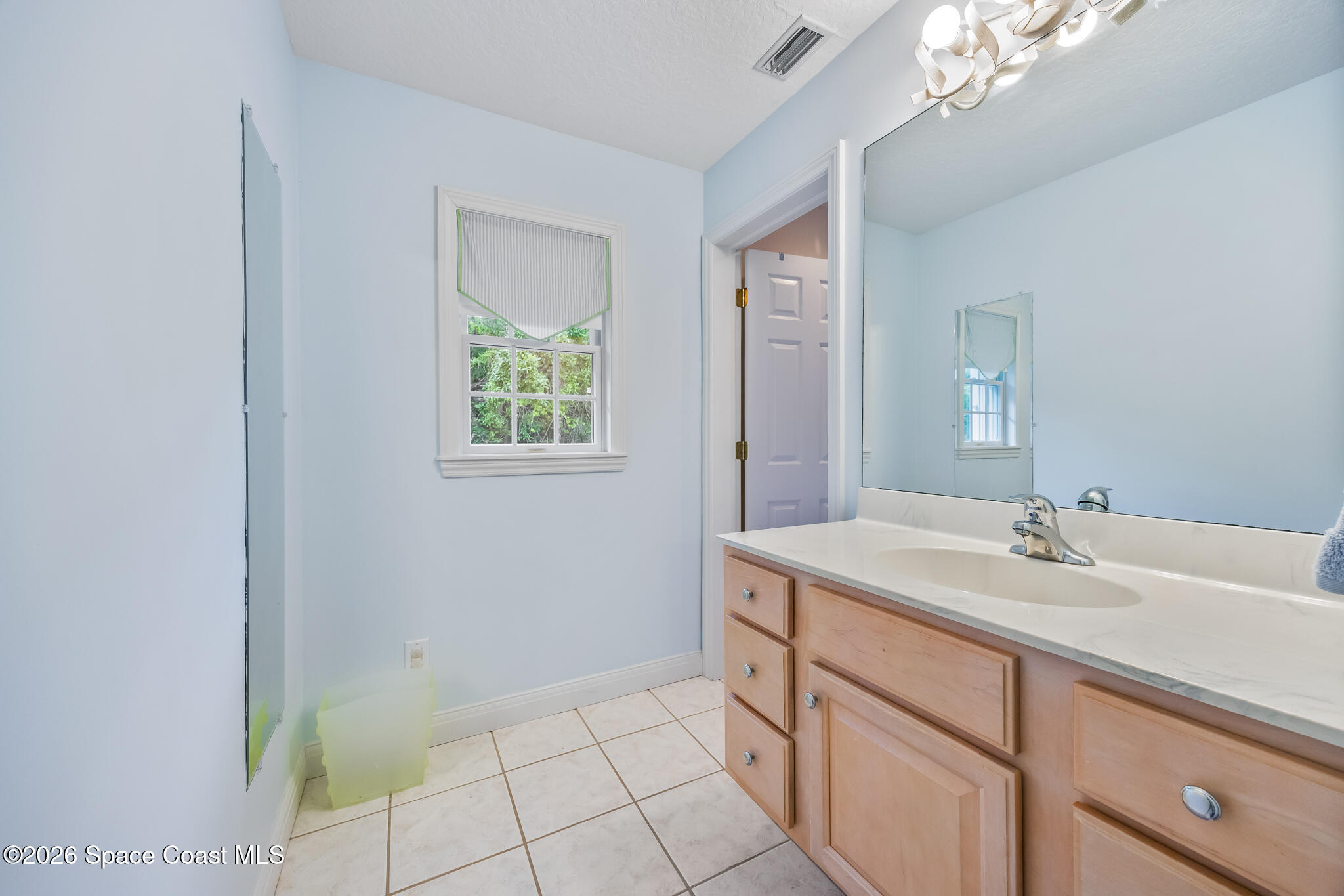 Bathroom with a light wood vanity, large mirror, tiled floor, and glass shower partition.