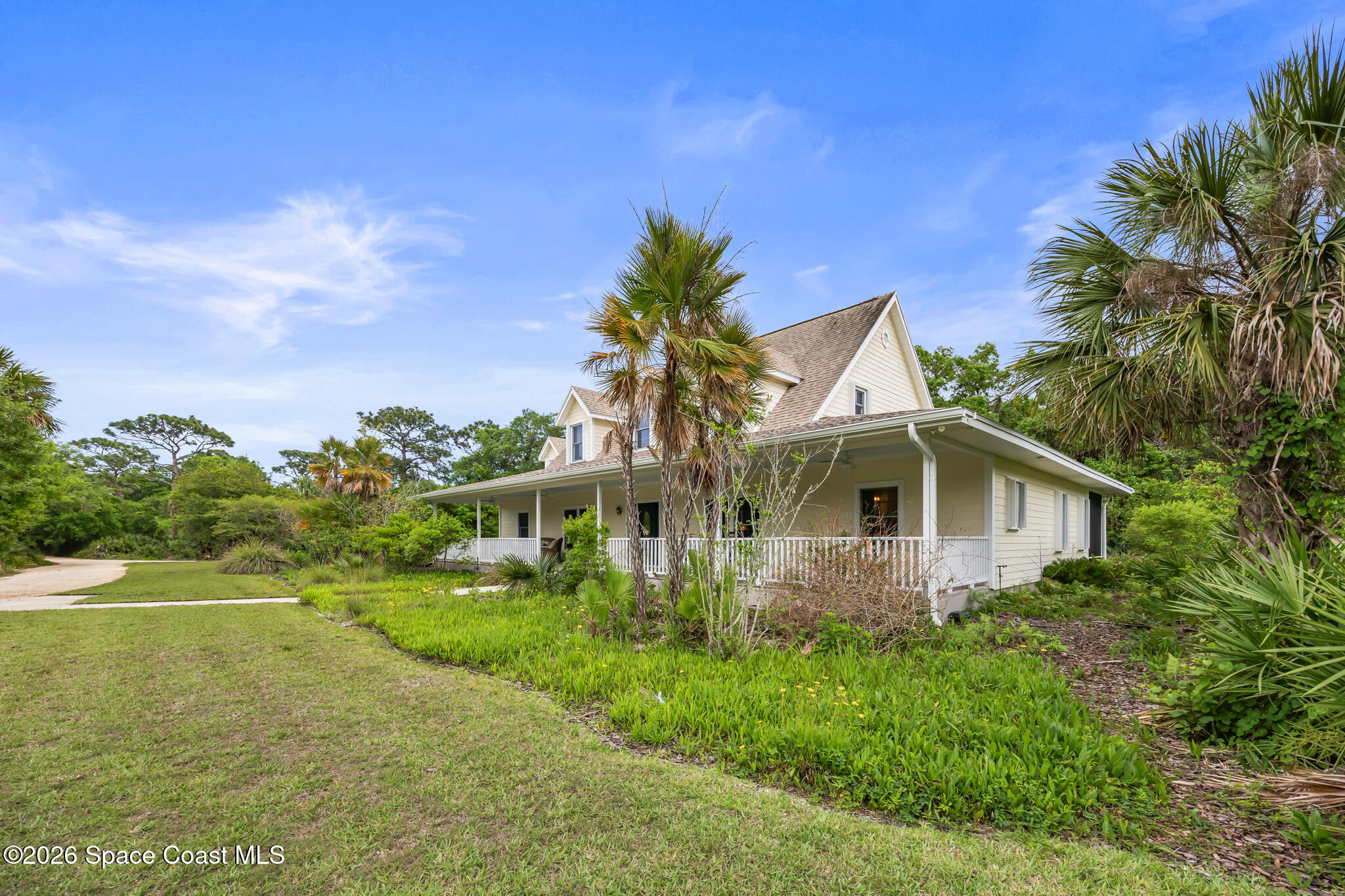 Two-story house with a covered wraparound porch, framed by palm trees and tropical landscaping.