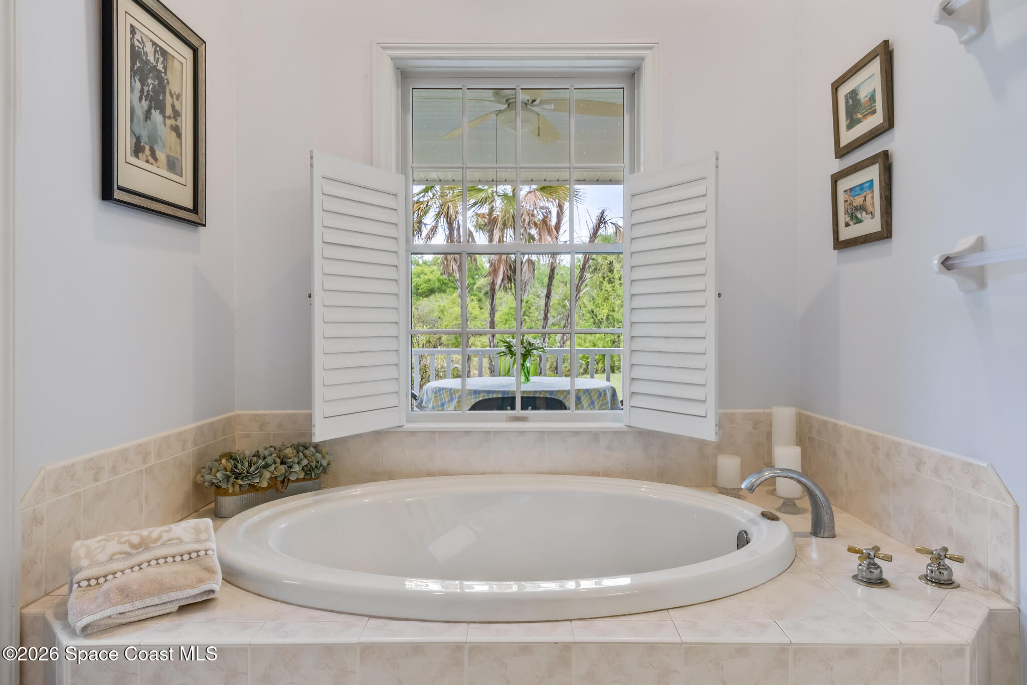 Bathroom with a large tiled-in soaking tub beneath a window overlooking palm trees.