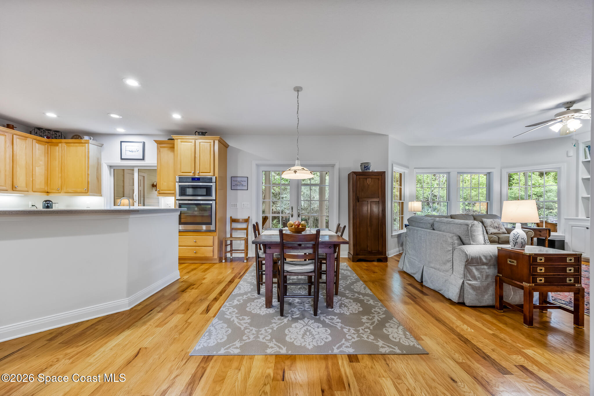 Open-plan kitchen, dining area, and living room with wood cabinets, hardwood floors, and large windows.