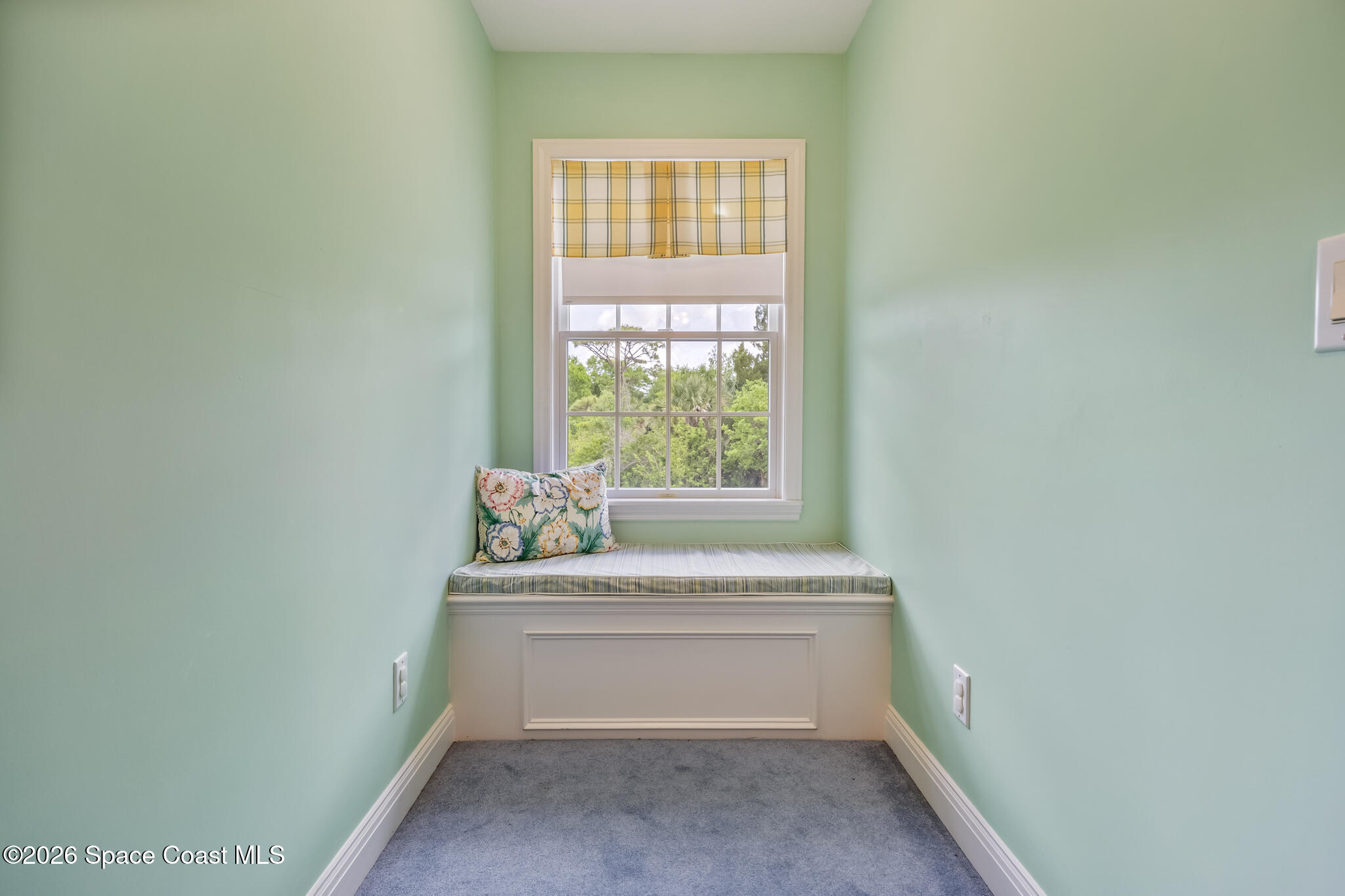 Mint-green nook with a built-in window seat, floral pillow, and window overlooking trees.