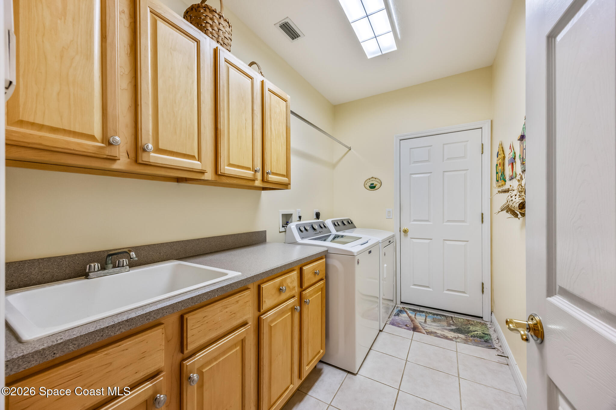 Laundry room with wood cabinets, utility sink, washer and dryer, and a skylight.