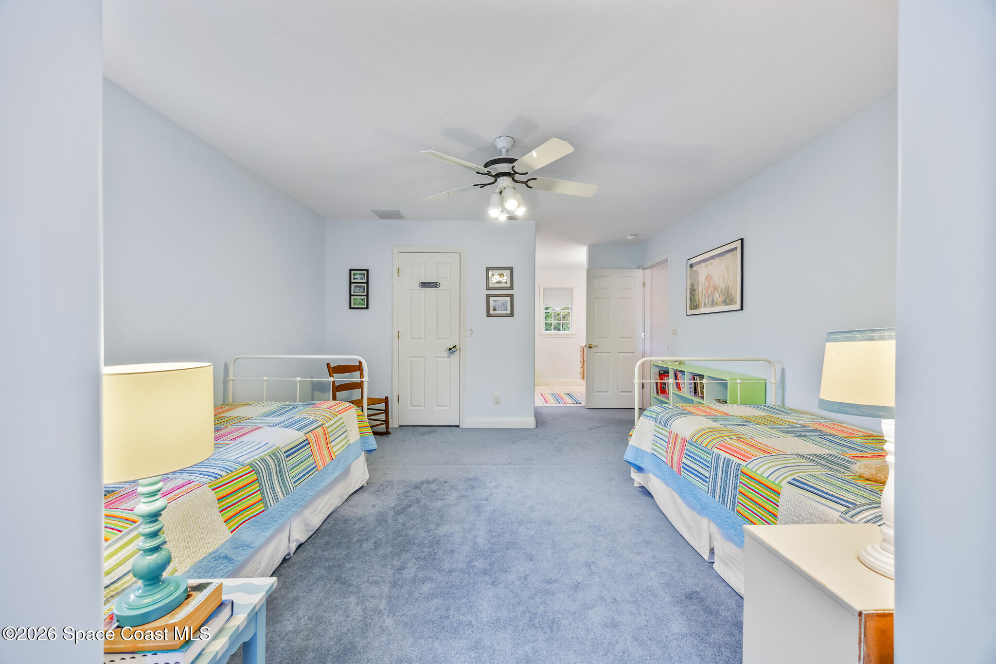 Bedroom with two twin beds in colorful striped quilts and blue carpet.