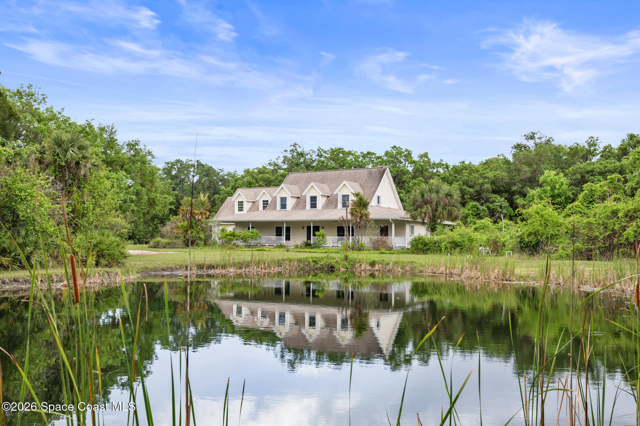 Two-story home with dormer windows and a covered porch reflected in a pond
