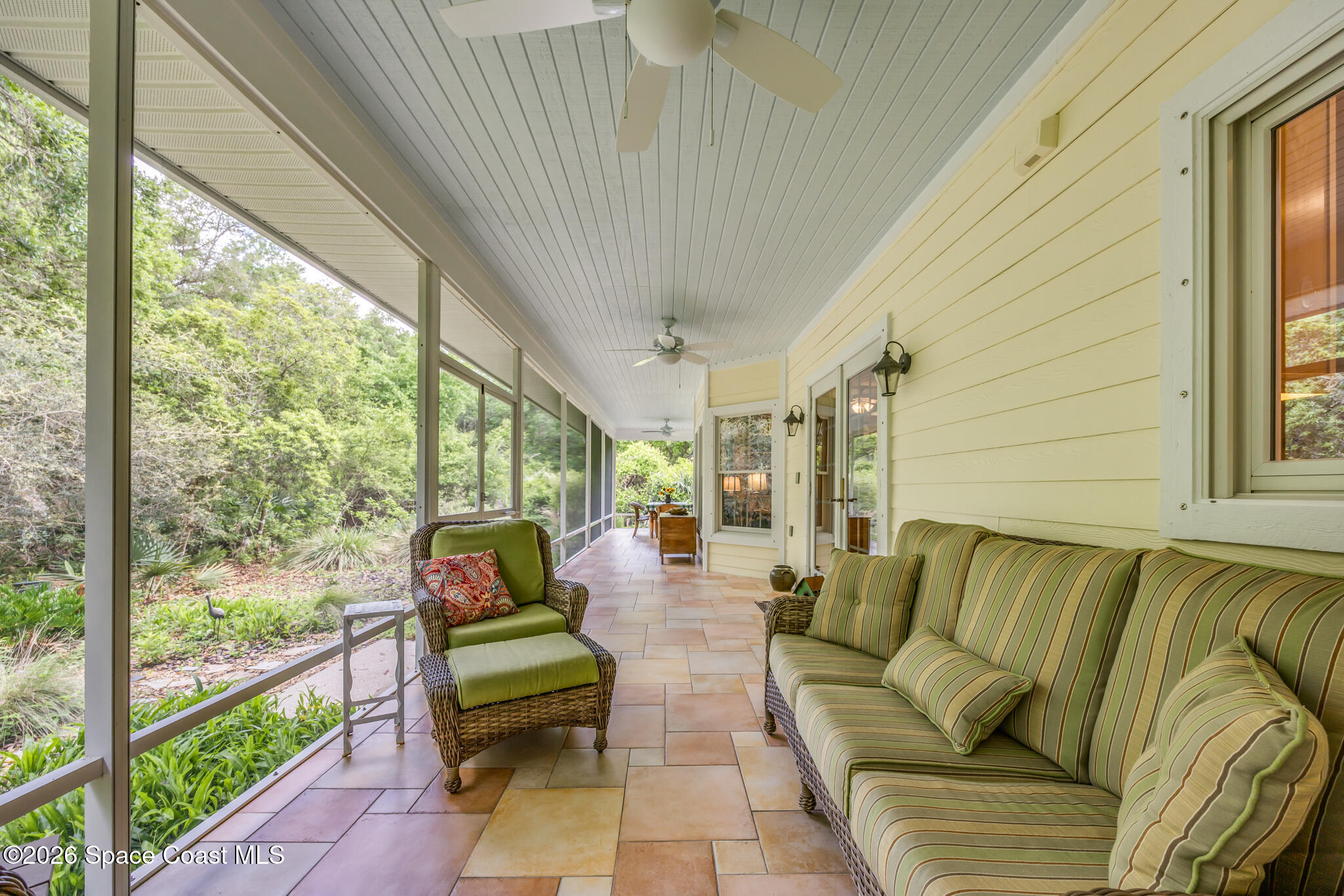 Screened porch with striped sofa, wicker lounge chair, tile floors, and leafy garden views.