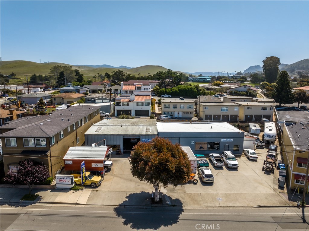 Aerial view of an auto repair shop, parking lot, and surrounding low-rise buildings with hills beyond.