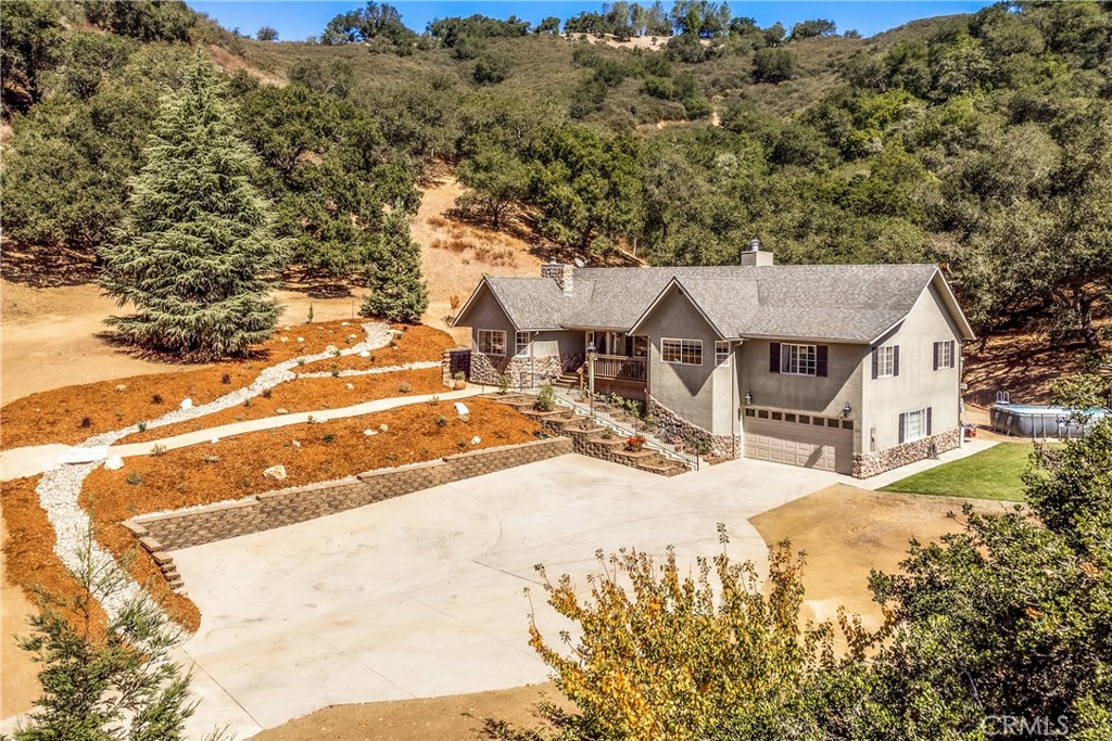 Gray two-story house with a broad driveway and hillside landscaping, viewed from above.