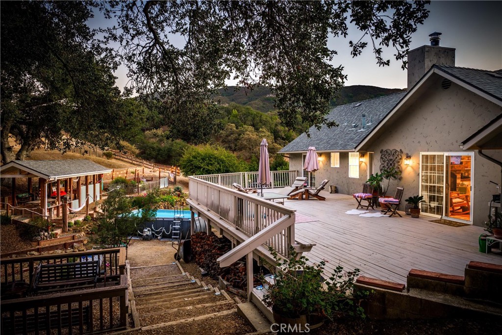 House with a spacious wooden deck, outdoor seating, small pool, and oak-covered hillside setting.