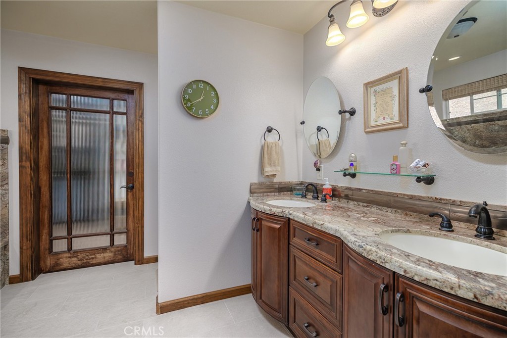 Bathroom with a double-sink wood vanity and stone countertop beside a frosted-glass door.