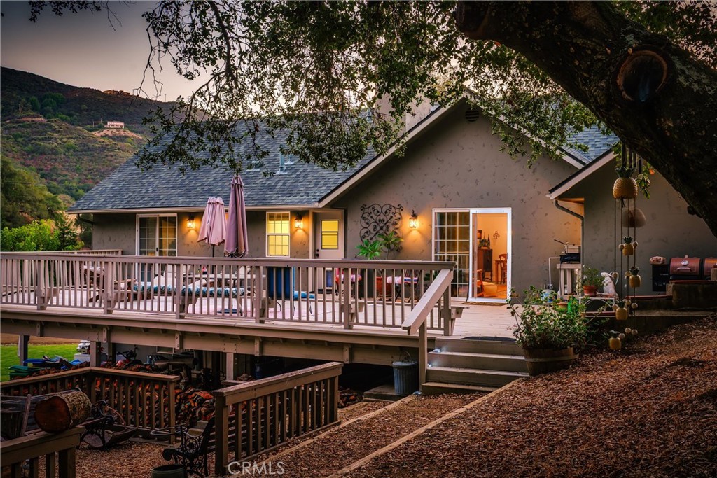 House at dusk with a broad raised deck, outdoor furniture, and wooded hills behind it.
