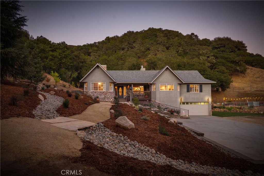 Gray stucco home with stone accents, a two-car garage, and a landscaped walkway at dusk.