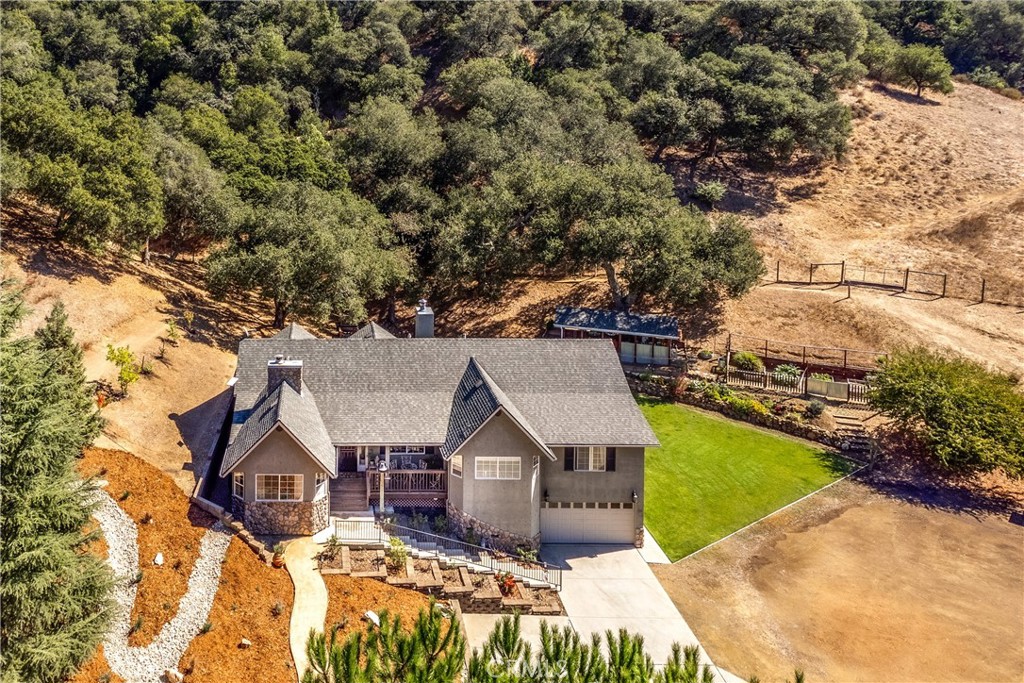 Aerial view of a home with a green lawn, driveway, and wooded acreage.