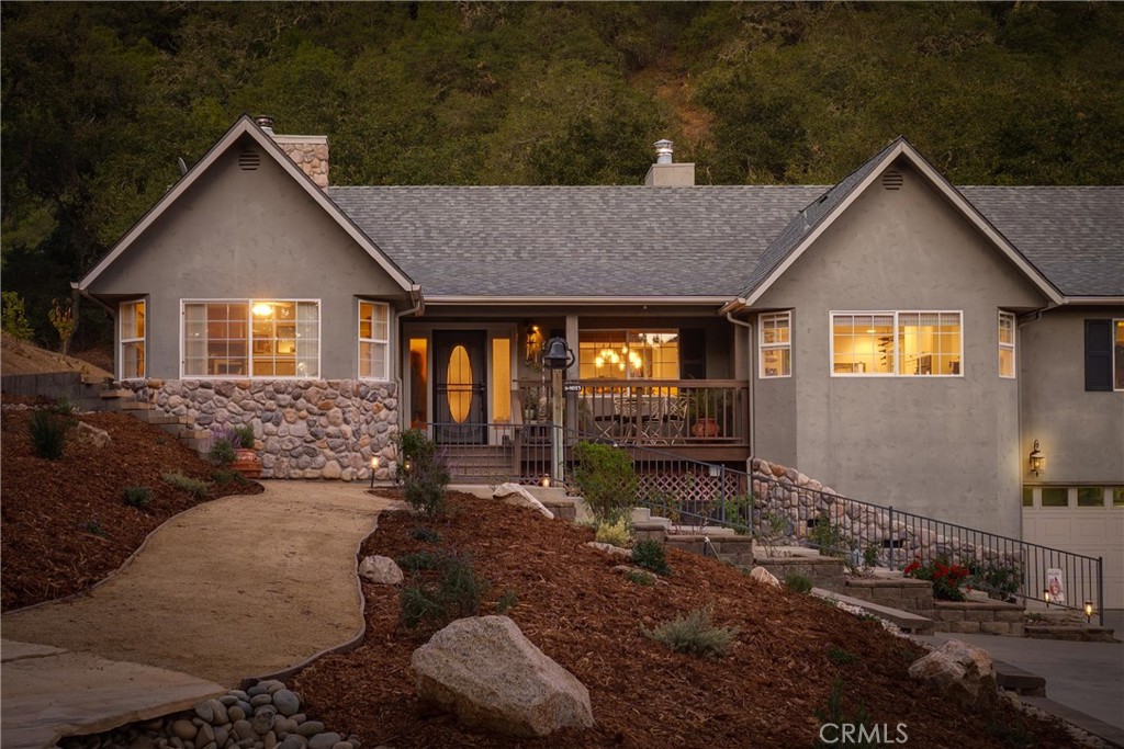 Gray stucco home with stone accents, a covered porch, and warmly lit windows at dusk.