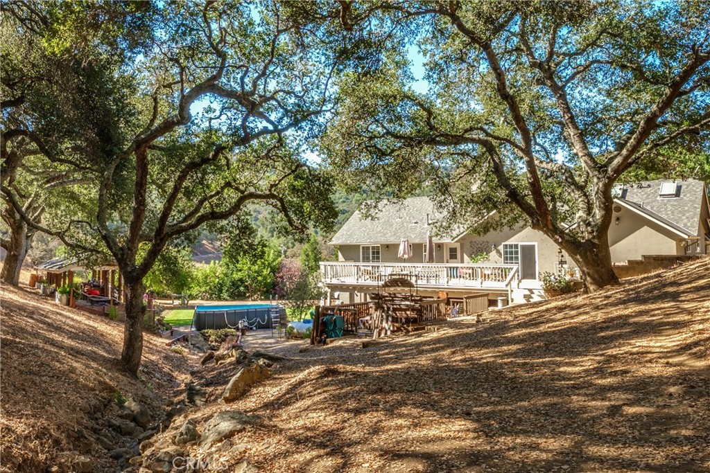 House with a raised deck and above-ground pool beneath mature oak trees on a sloping lot.