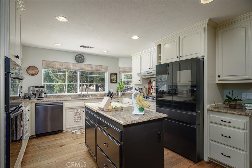 Kitchen with a granite island, dark appliances, white cabinetry, and large windows overlooking trees.