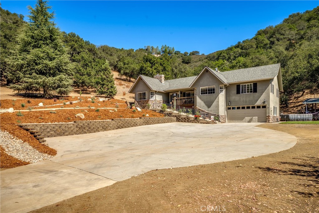Gray hillside home with an attached garage, broad concrete driveway, and terraced landscaping.