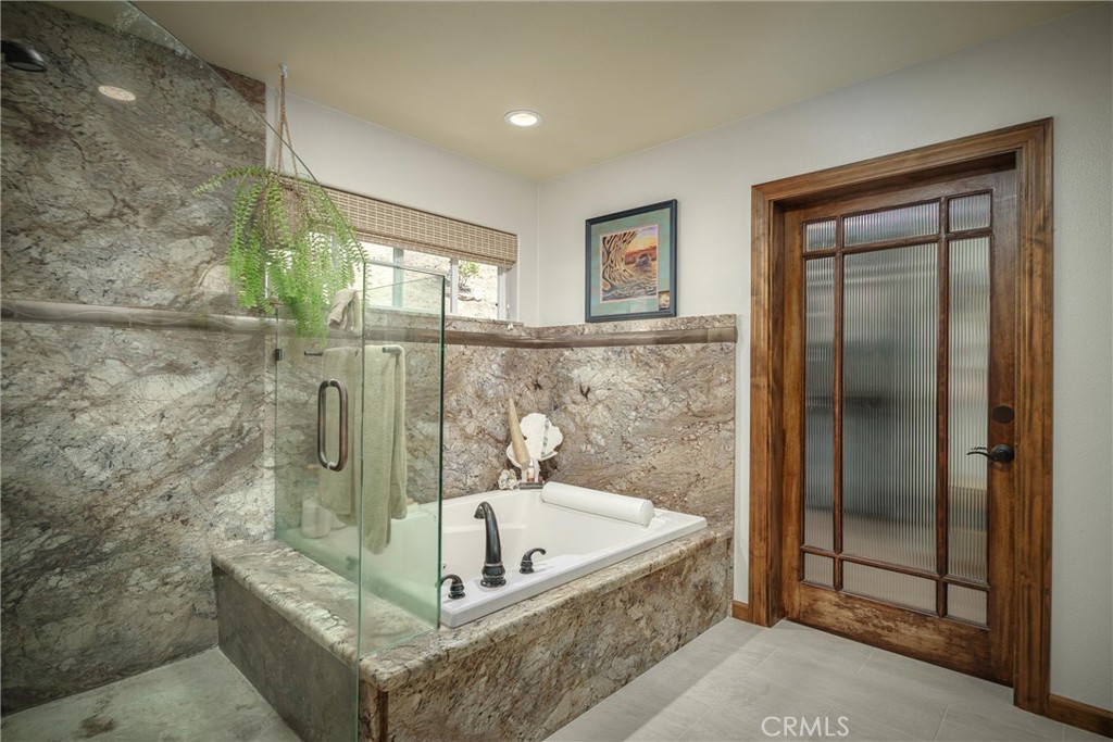 Bathroom with a stone-surrounded soaking tub, glass shower partition, and wood-framed frosted-glass door.