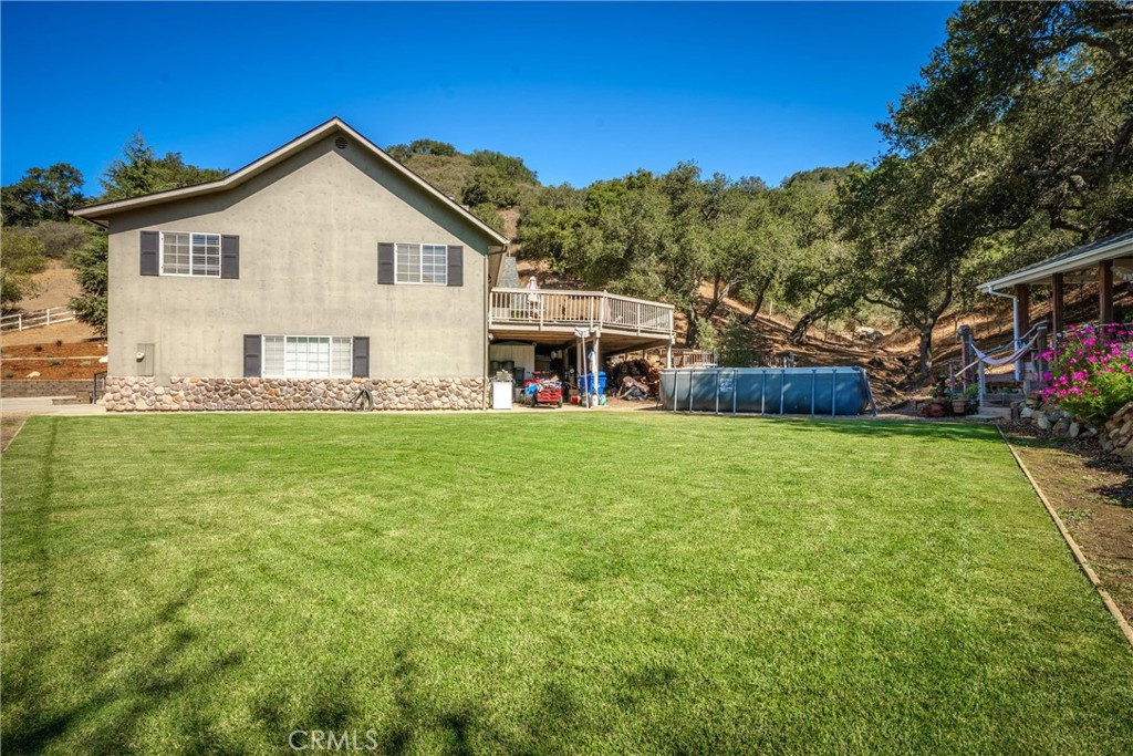 House with a raised deck, above-ground pool, and broad lawn against wooded hills.